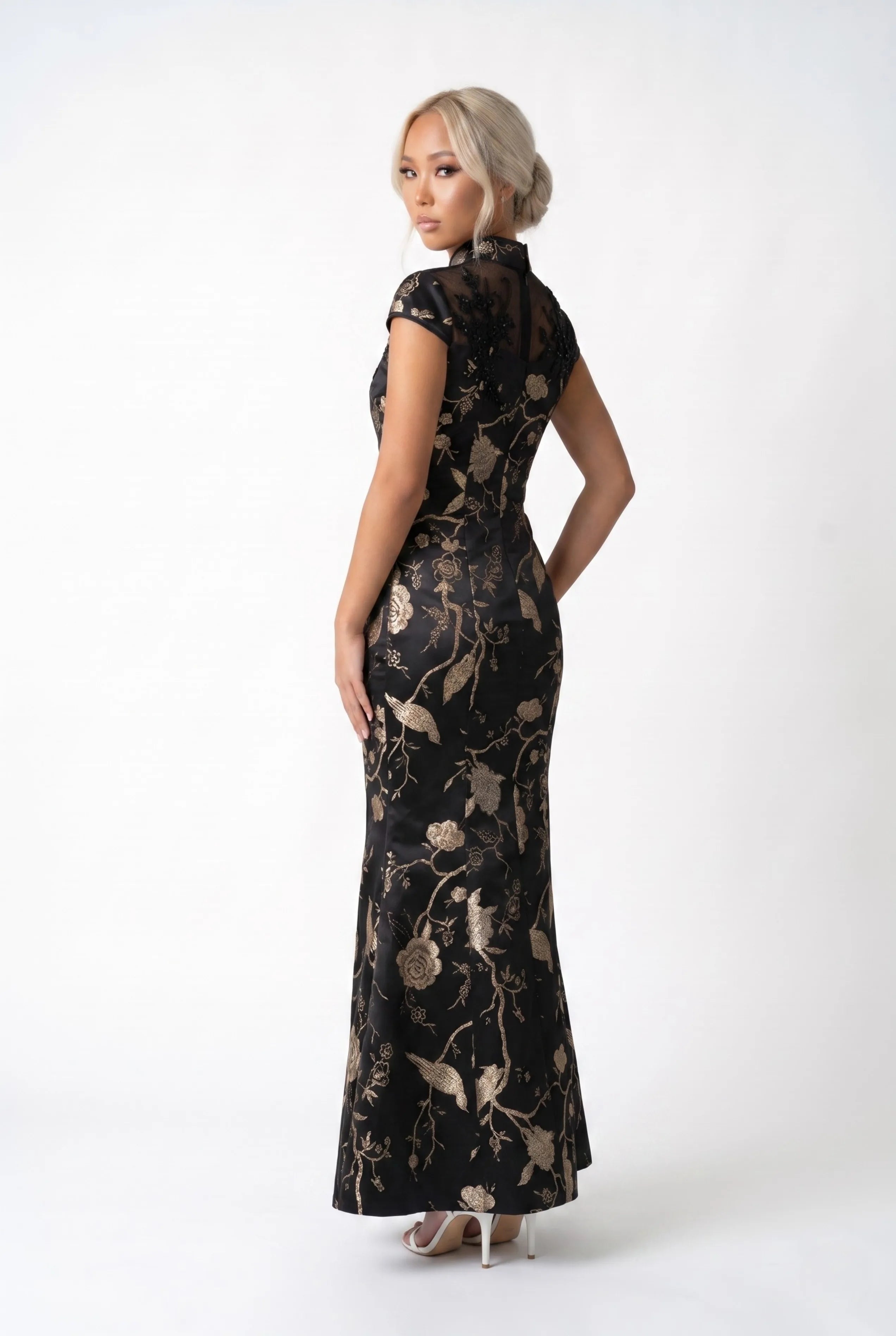 Three-quarter back profile view highlighting the form-fitting silhouette of the long black and gold qipao