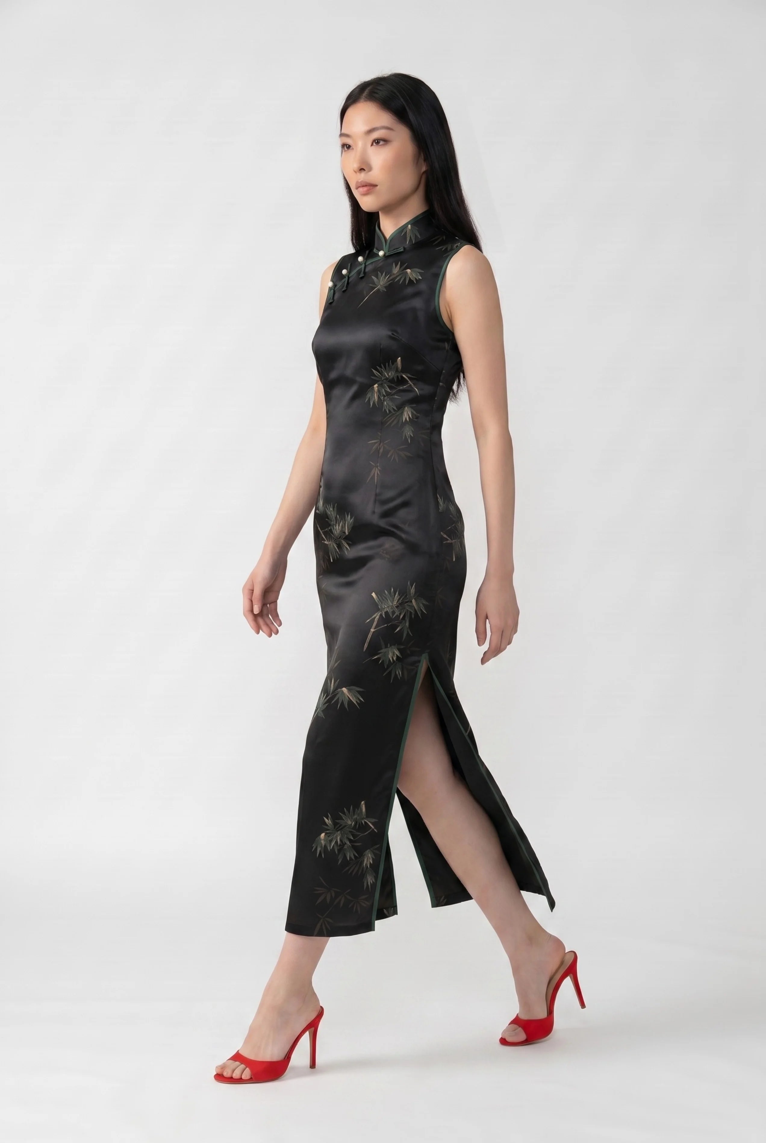 Full-body side profile view of a woman in stride wearing the black cheongsam dress with a green bamboo pattern