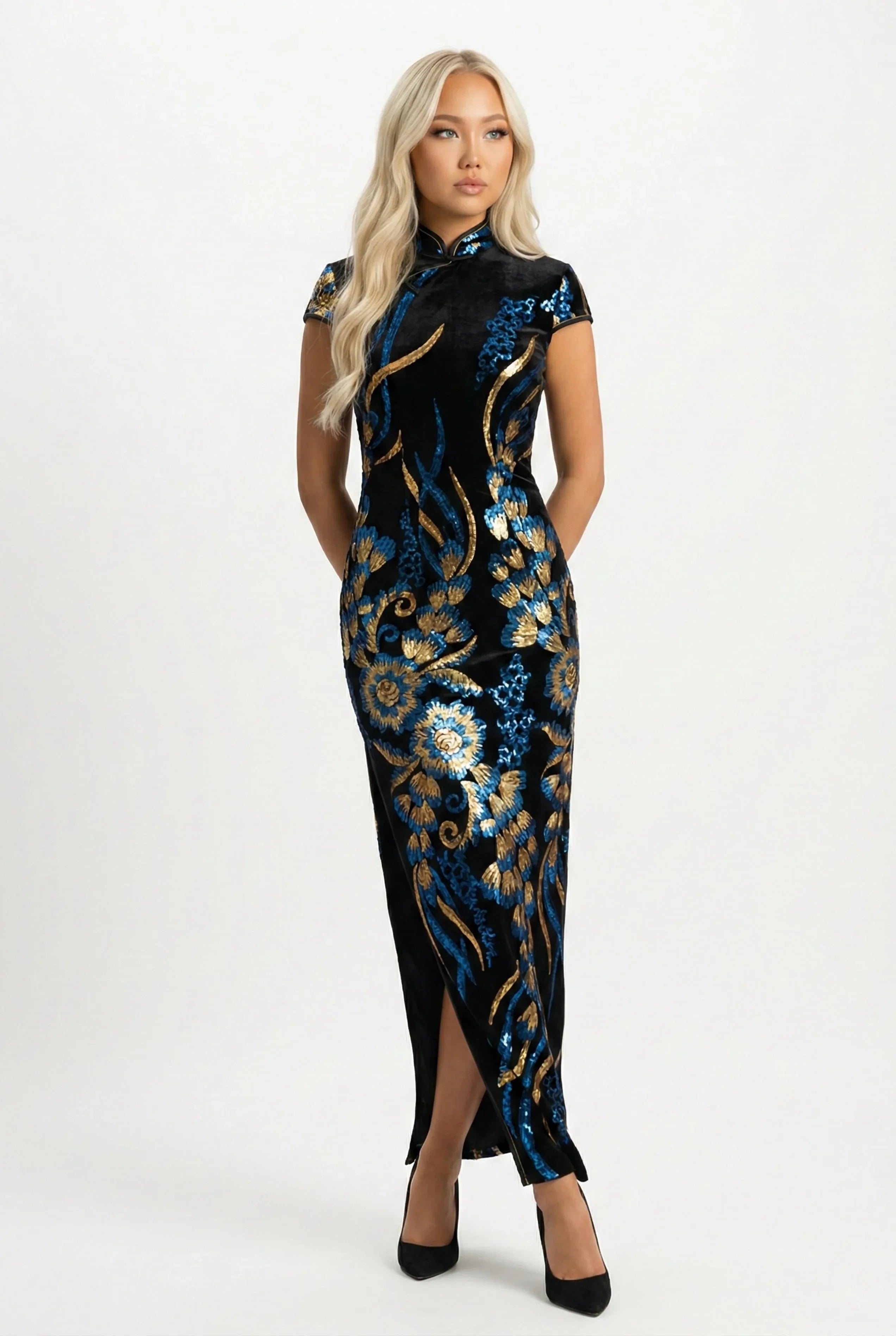 A woman with blonde hair posing in a long black velvet qipao dress featuring vibrant blue and gold floral sequin embroidery