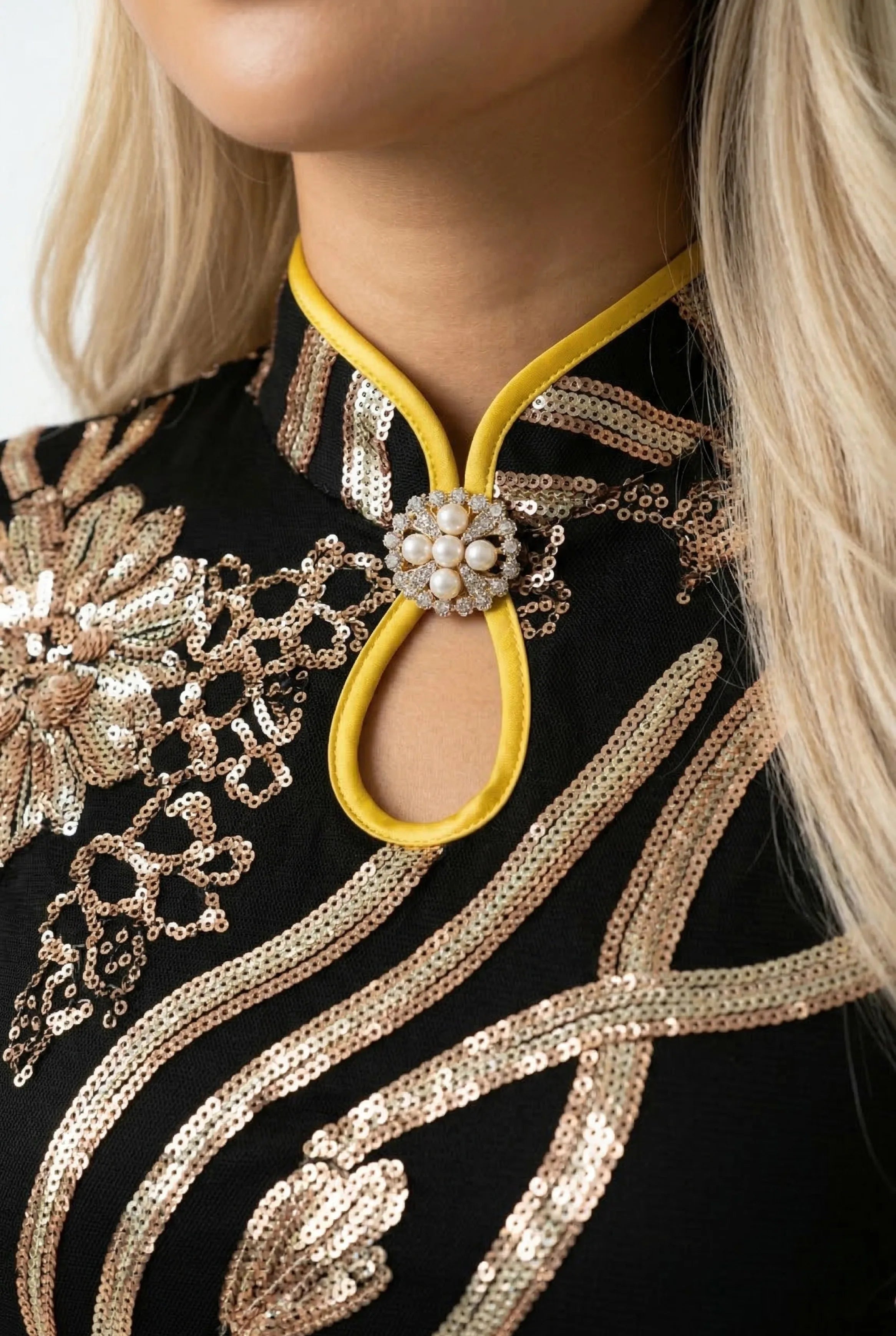Close-up of the mandarin collar with yellow piping and a crystal flower brooch on a black and gold sequin dress.
