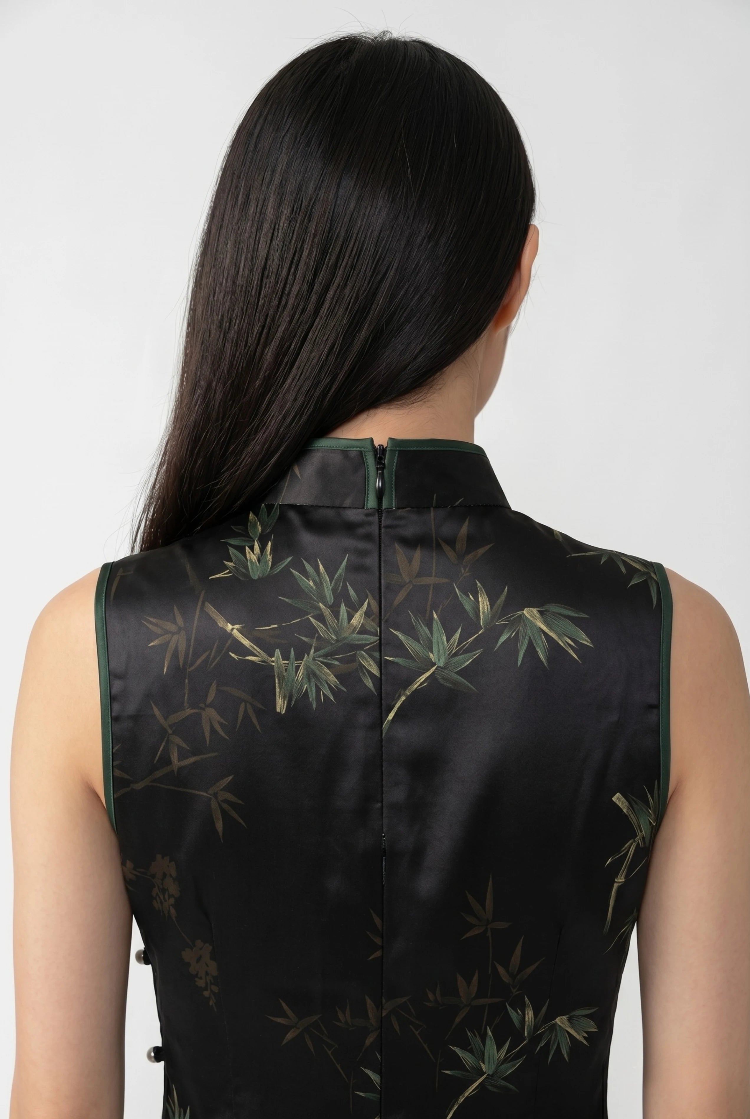 Close-up back view showing the hidden zipper closure, high collar structure, and green bamboo pattern on the black satin