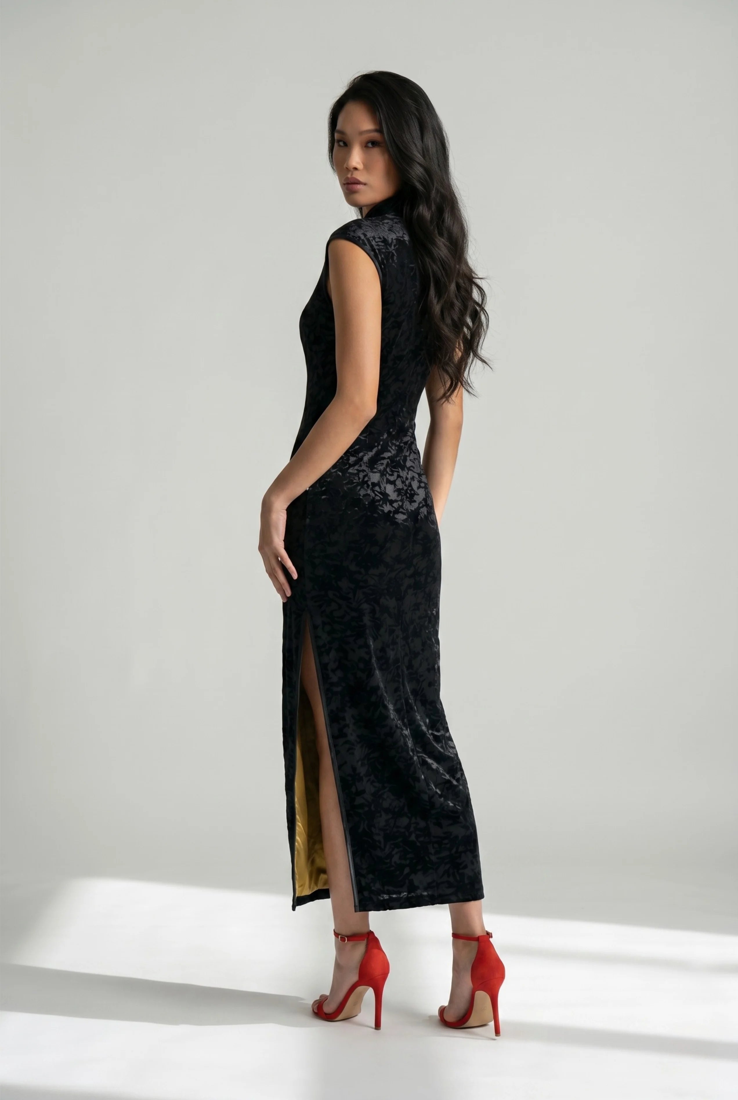 Three-quarter back view of the black velvet qipao, highlighting a high side slit with contrasting gold fabric lining.