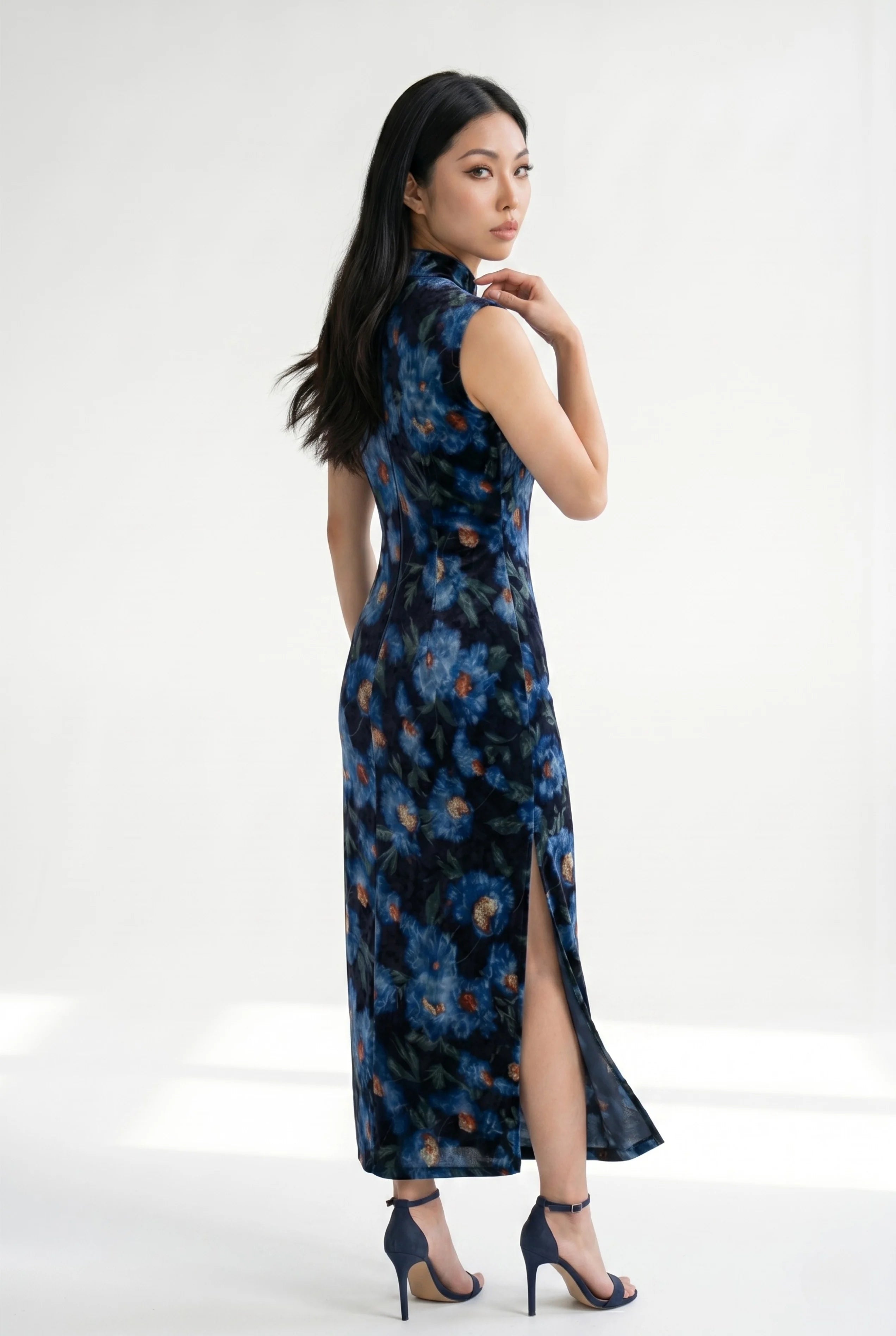 Three-quarter back profile view of a woman posing in the blue floral velvet qipao dress