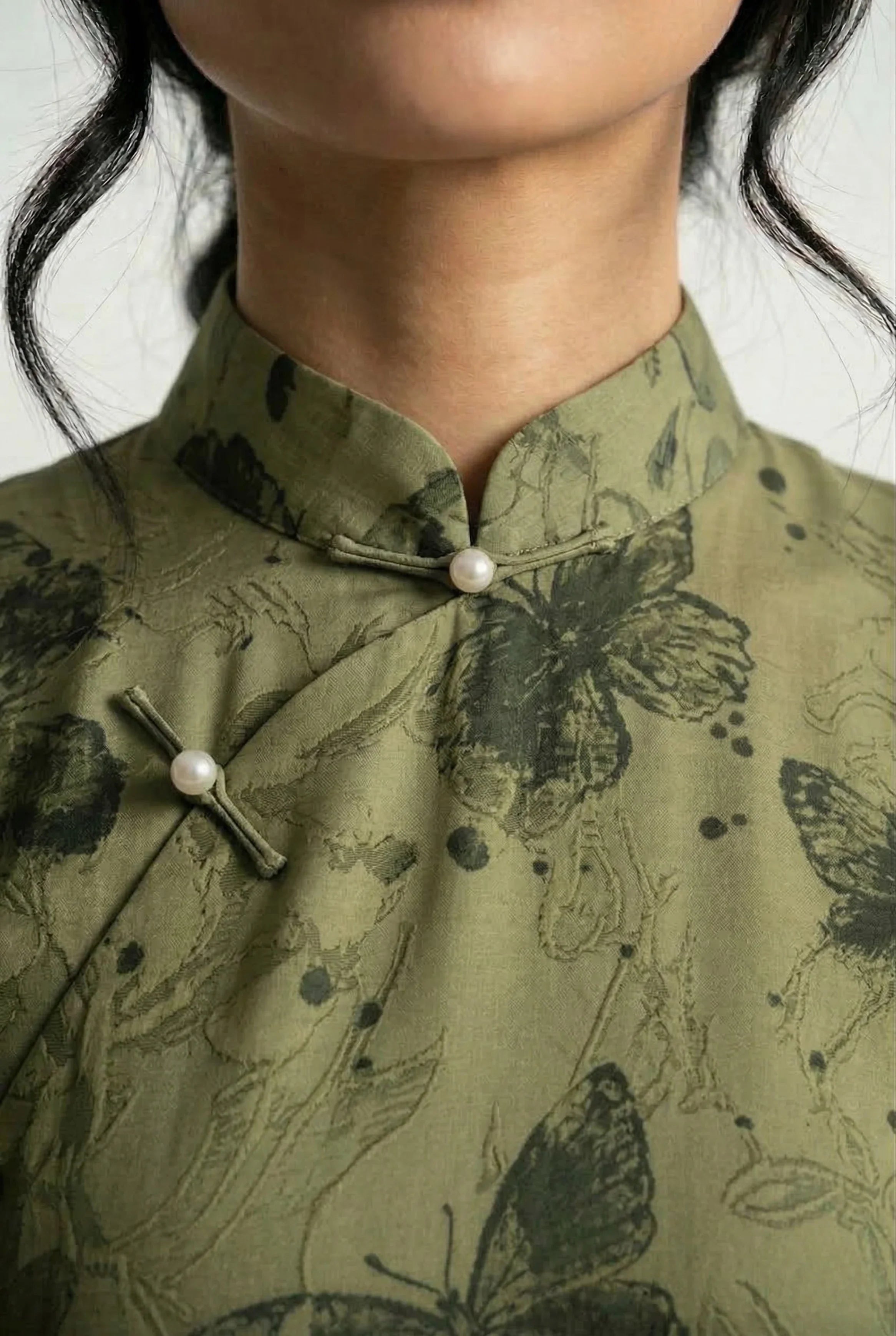 Close-up of the mandarin collar on a butterfly print Qipao with a delicate pearl button closure.