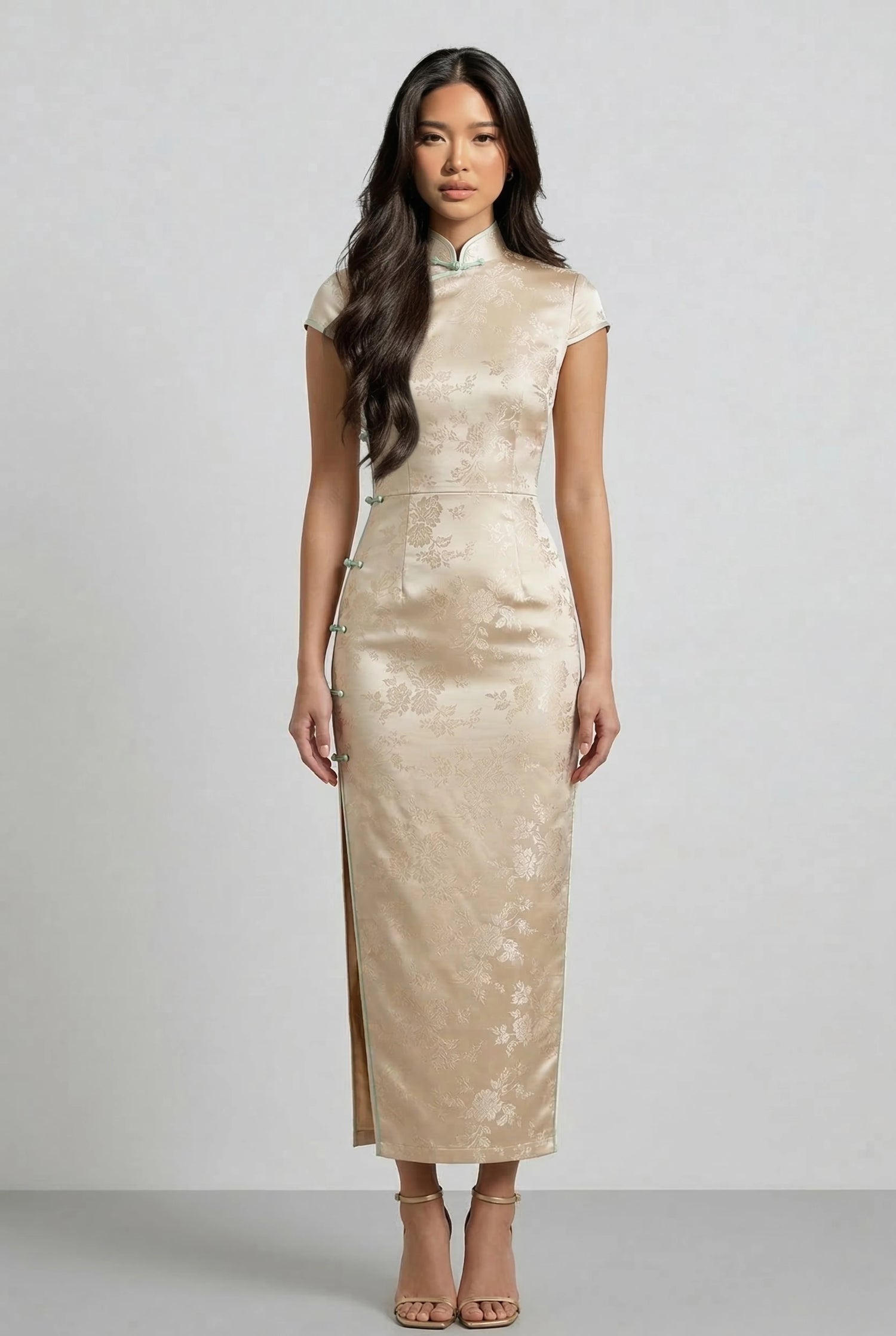 A model wearing a champagne gold mulberry silk qipao by Maison Hua, featuring a subtle floral brocade pattern, cap sleeves, and a traditional high Mandarin collar for a luxurious and elegant look