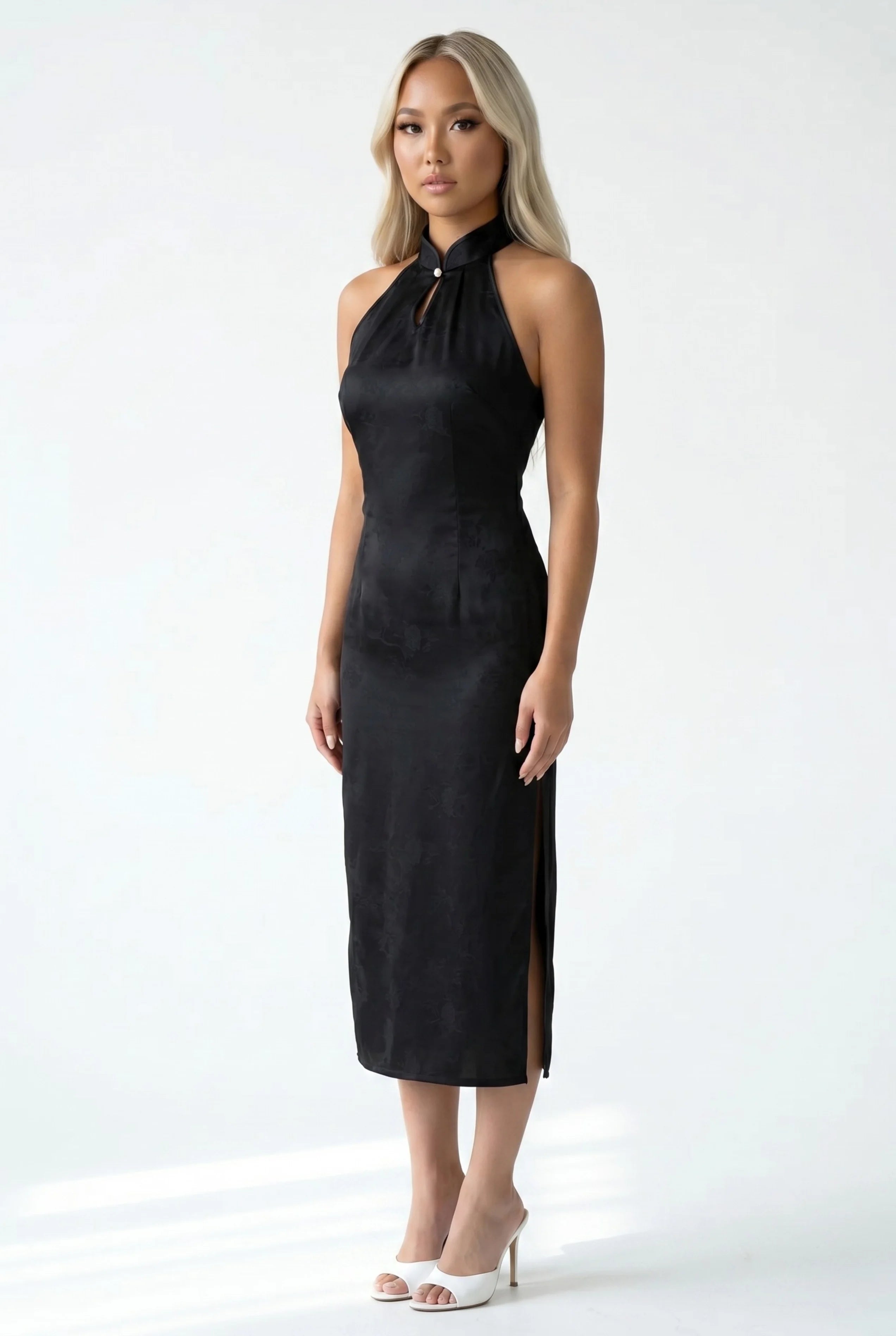 Front full-length view of a halter neck black cheongsam with a subtle floral jacquard pattern and white heels