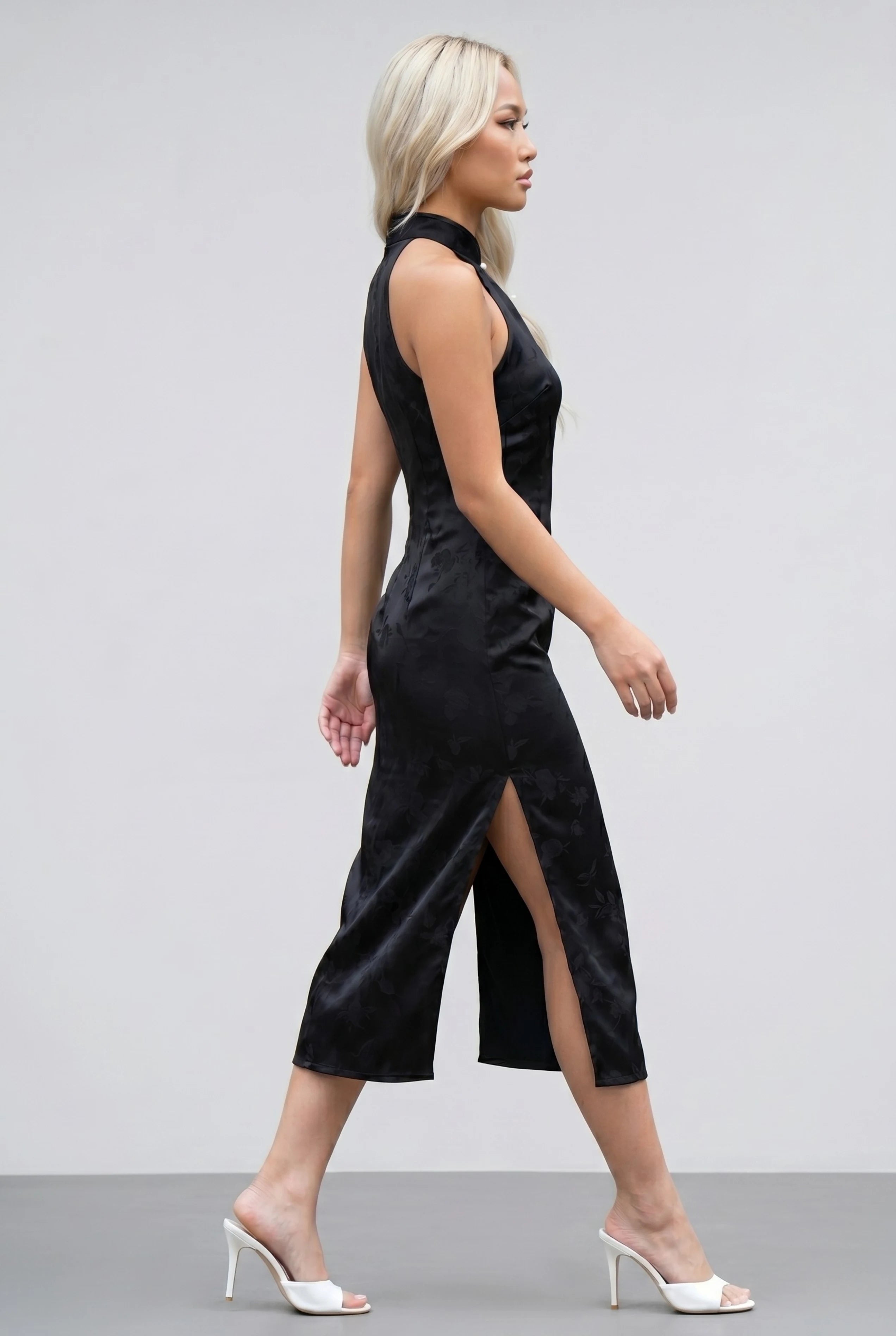 Side profile view of a woman walking in the black floral cheongsam dress, showcasing the high side slit