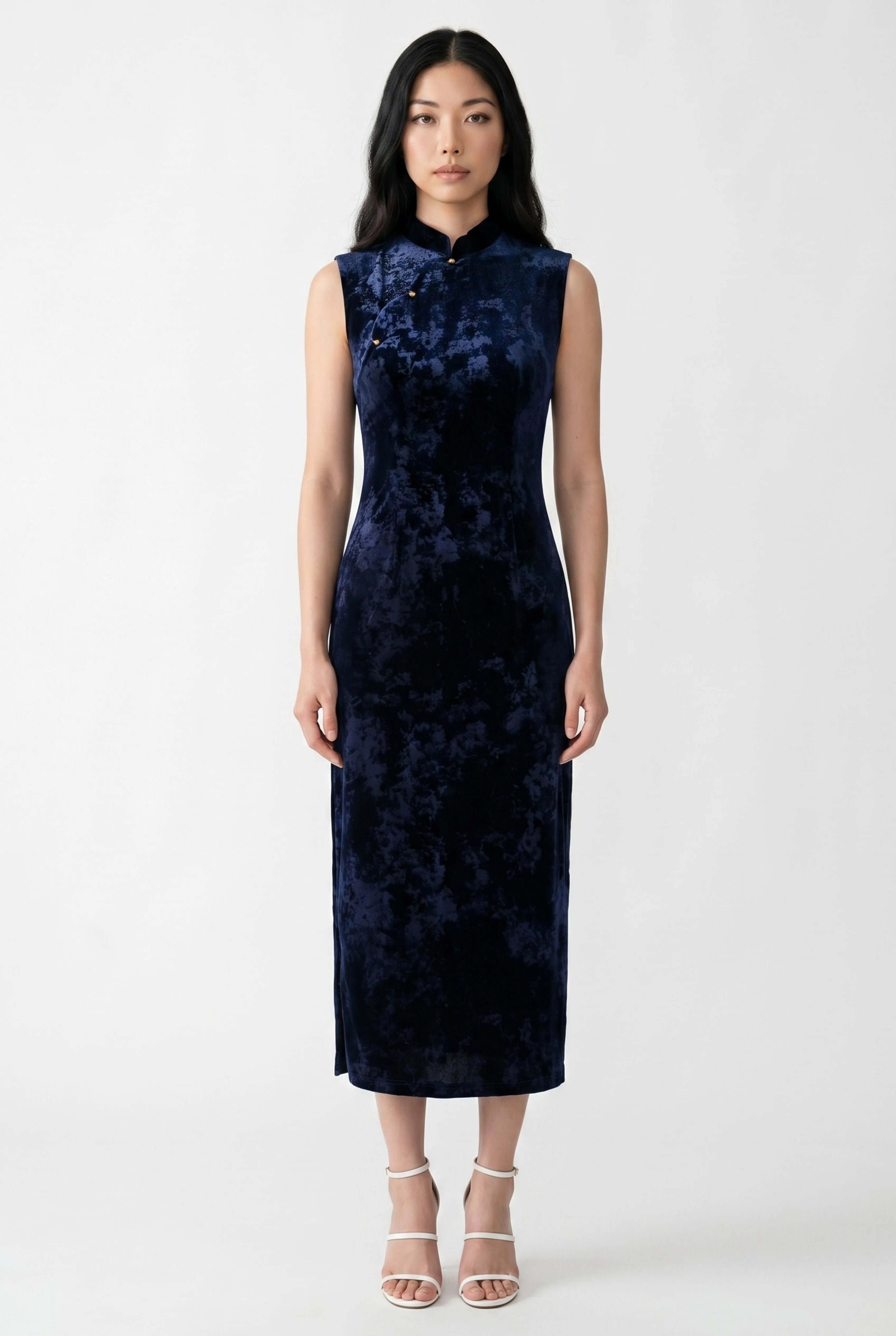 Front view of a sleeveless dark blue velvet cheongsam dress paired with white strappy heels