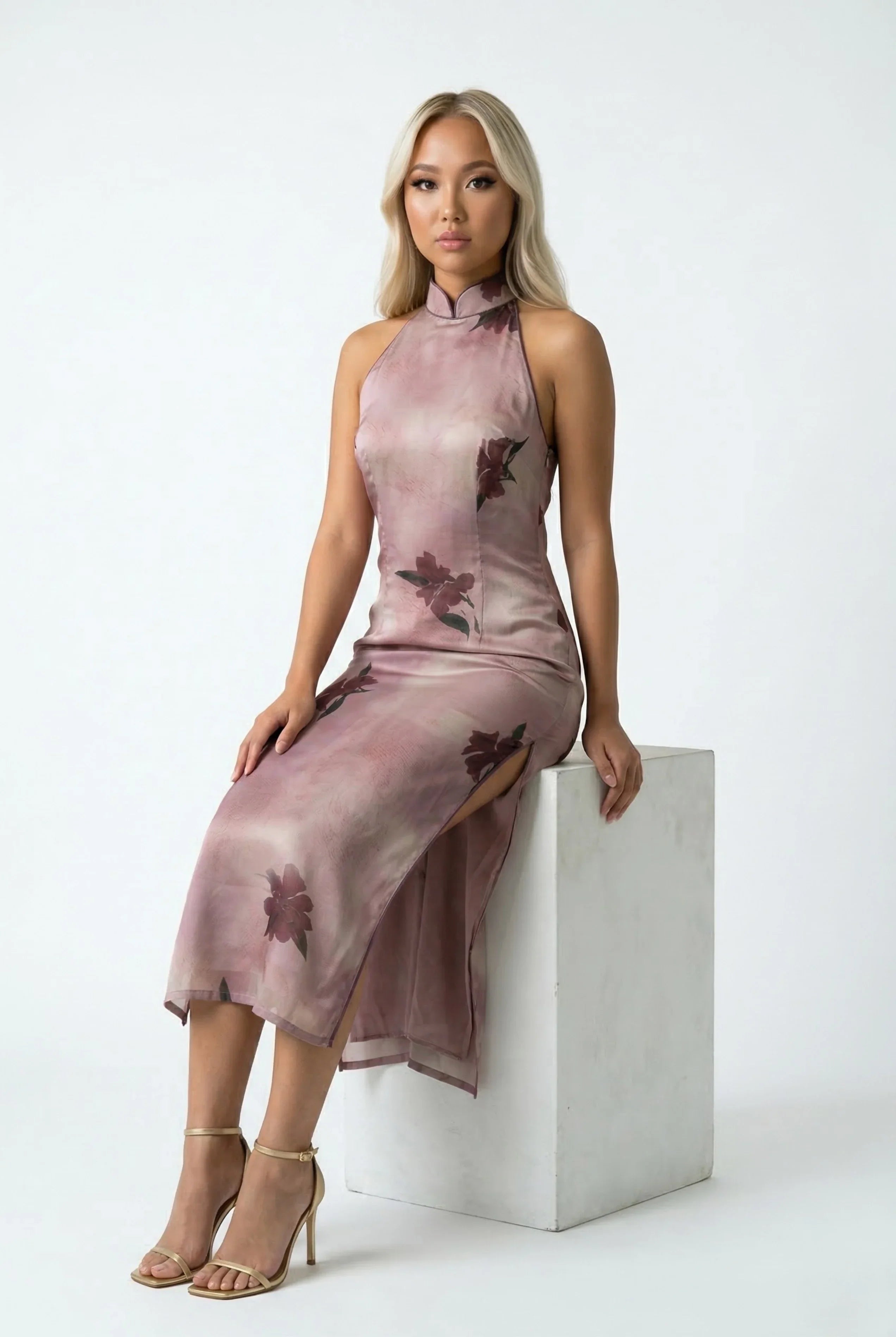Seated pose of a model wearing a dusty pink floral Qipao dress, highlighting the fabric's sheen and side slit.