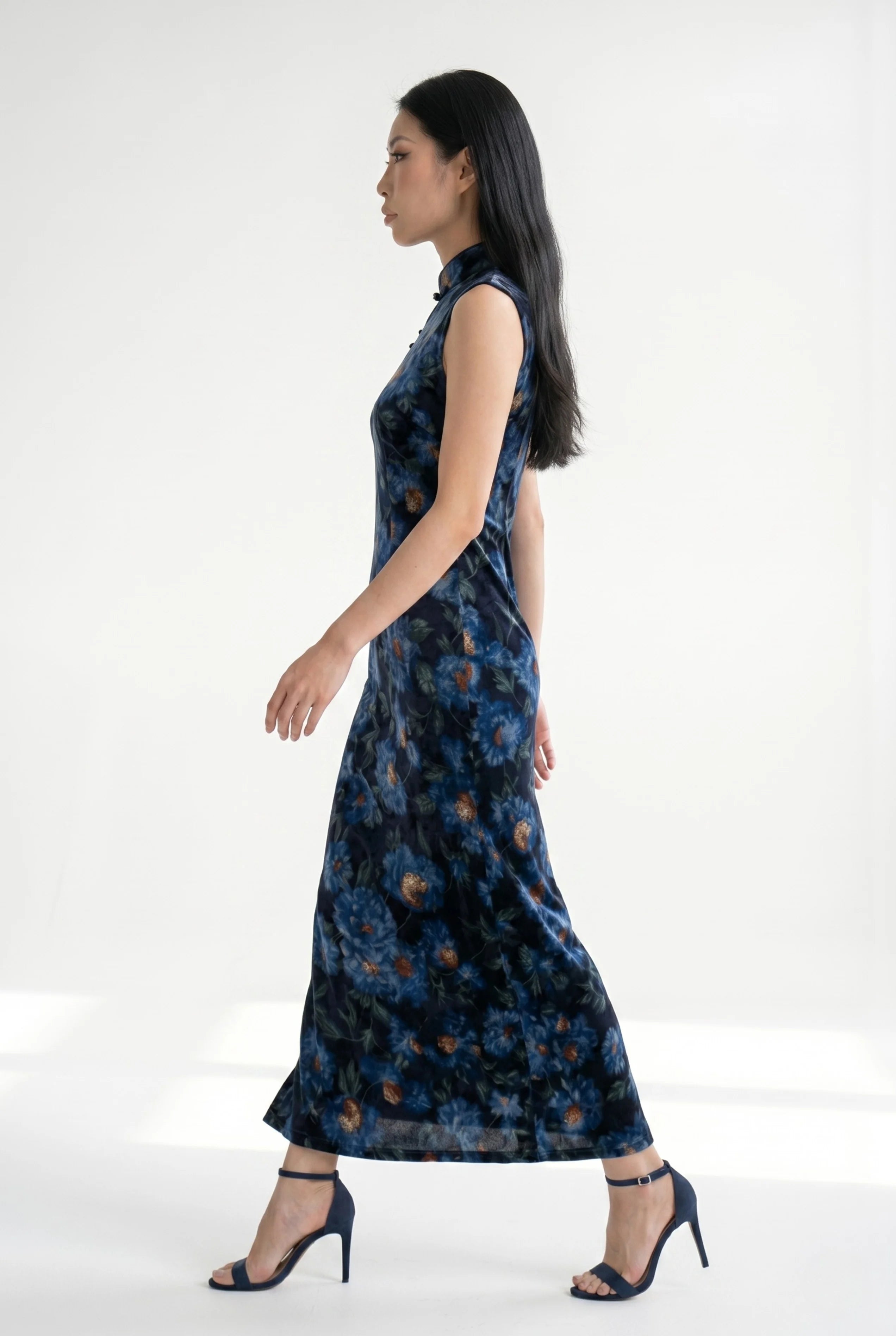 Side view of a woman striding in the floral velvet cheongsam dress, highlighting the movement and leg slit