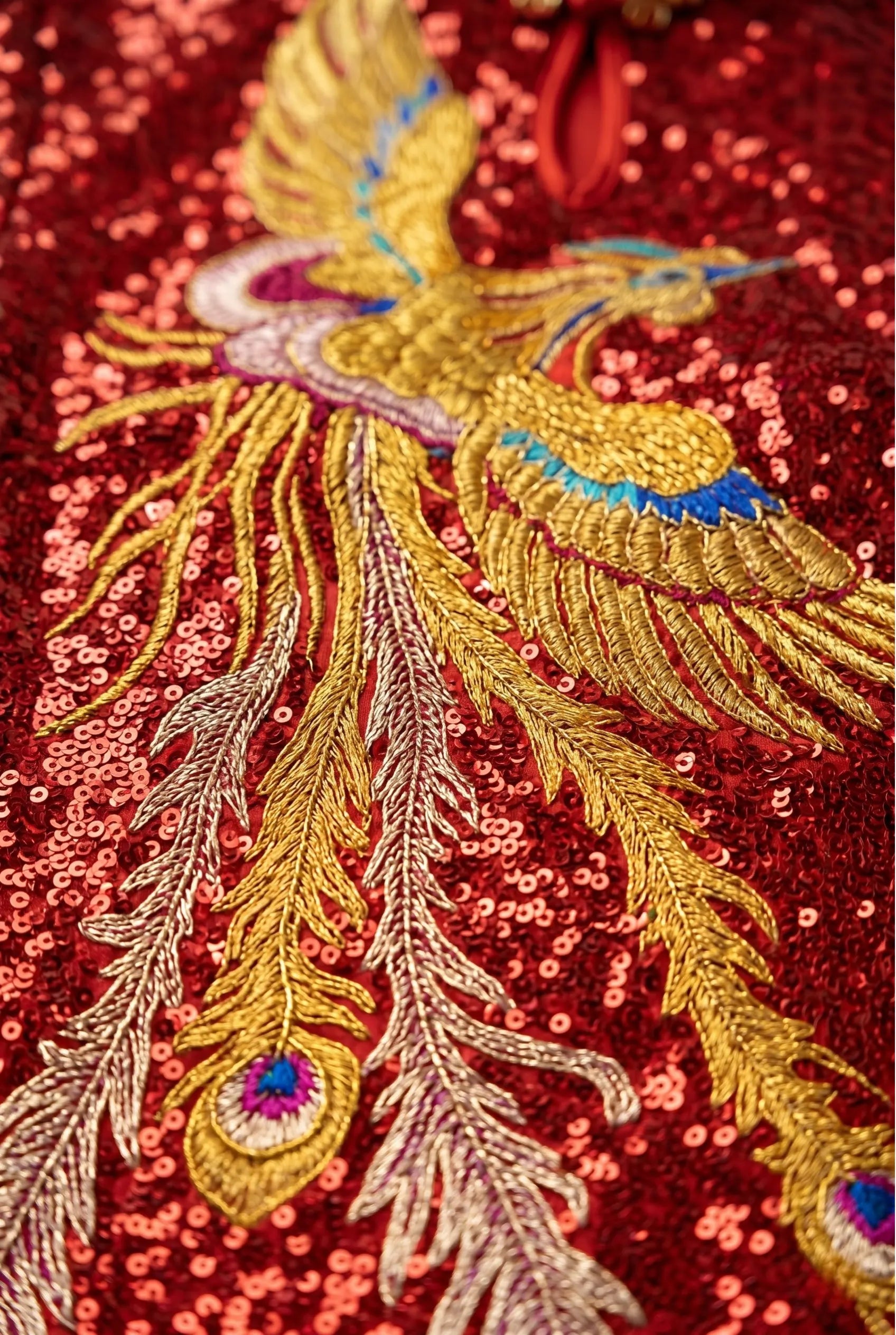 Macro close-up view of the intricate, colorful gold phoenix embroidery on the red sequin qipao.