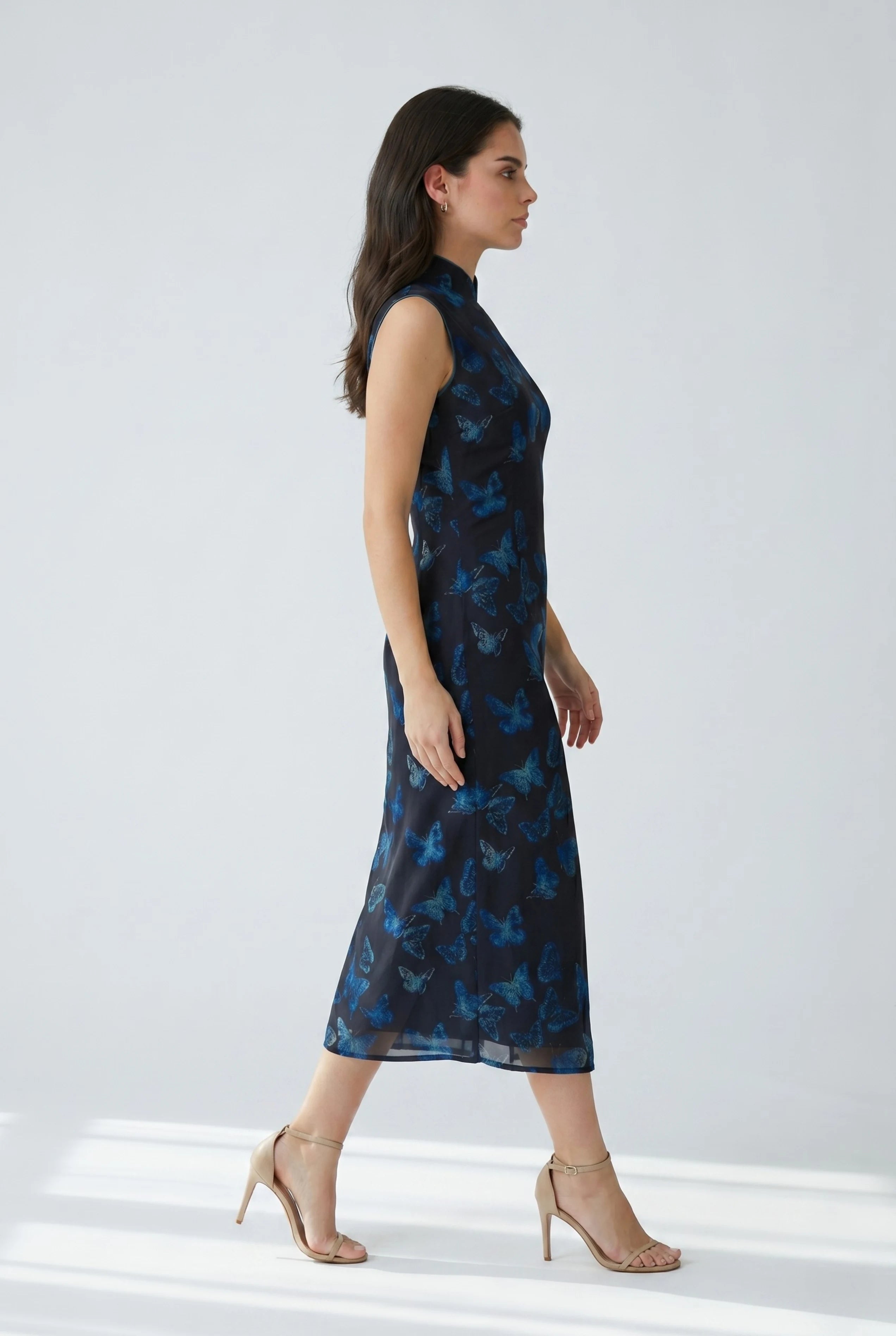 Full-body side view of a woman in stride wearing the green butterfly cheongsam dress paired with nude heels