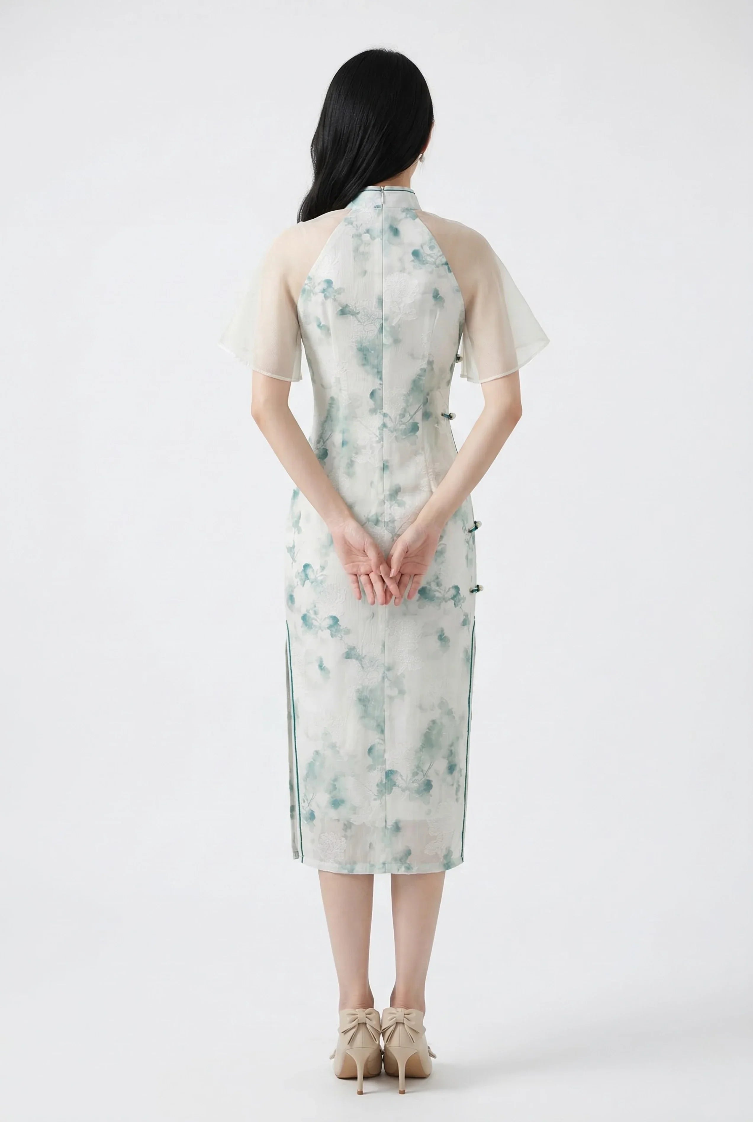 Back view of a form-fitting midi Qipao in a green floral print, highlighting the feminine silhouette and sheer shoulder detail.