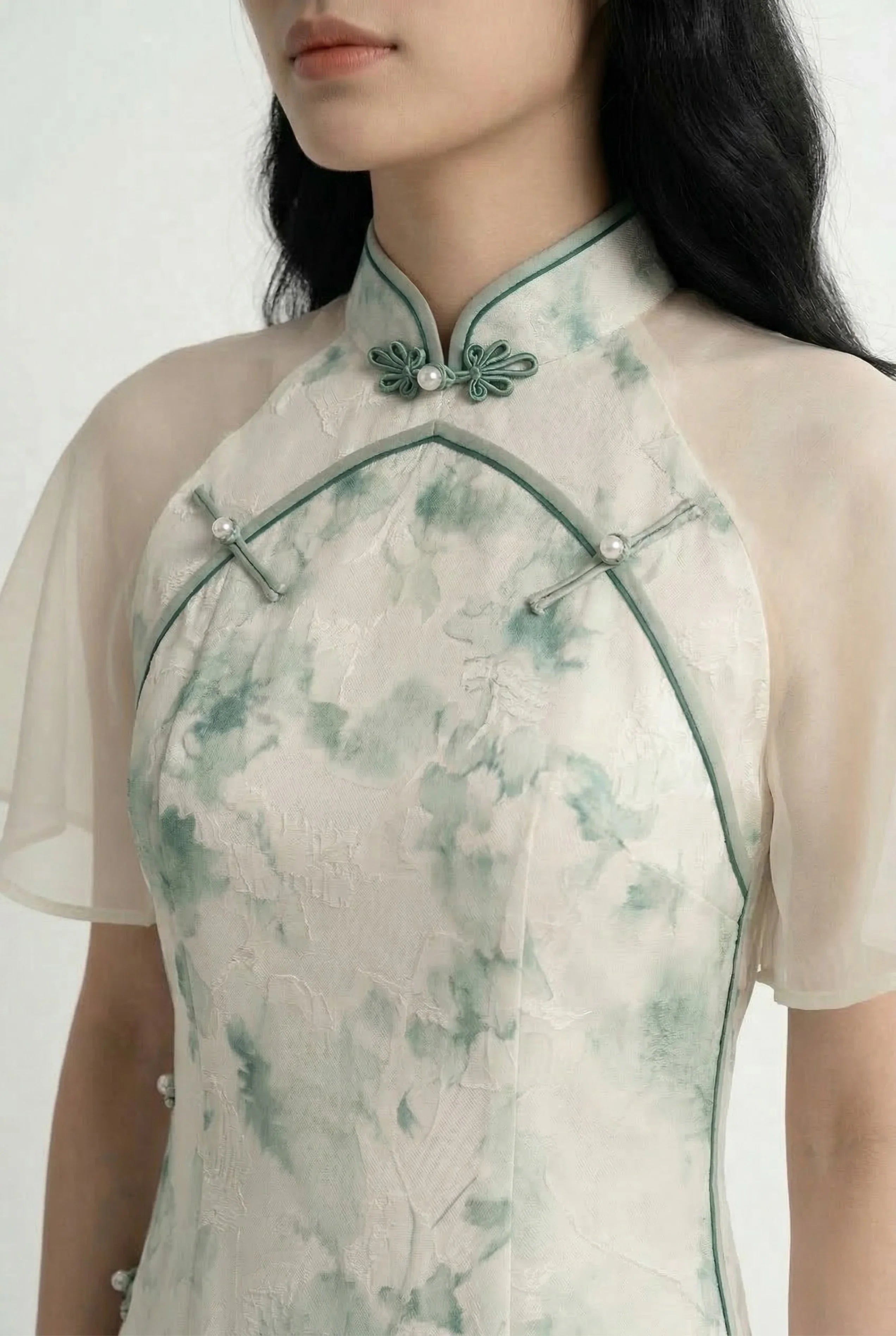Detailed shot of the green piping and traditional frog button closure on a watercolor floral print Qipao.