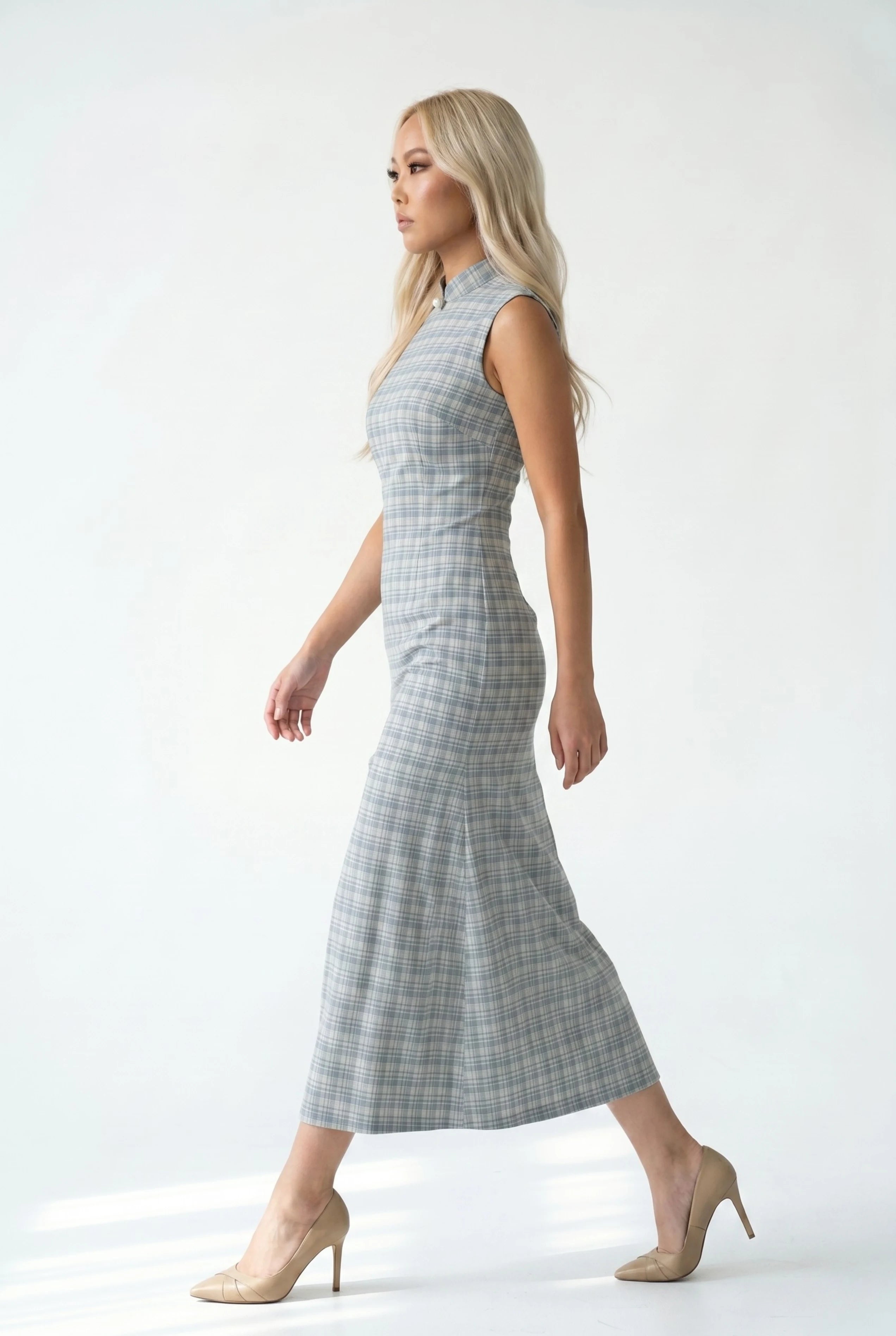 Full-body side view of a woman in stride wearing the grey plaid cheongsam dress paired with nude heels