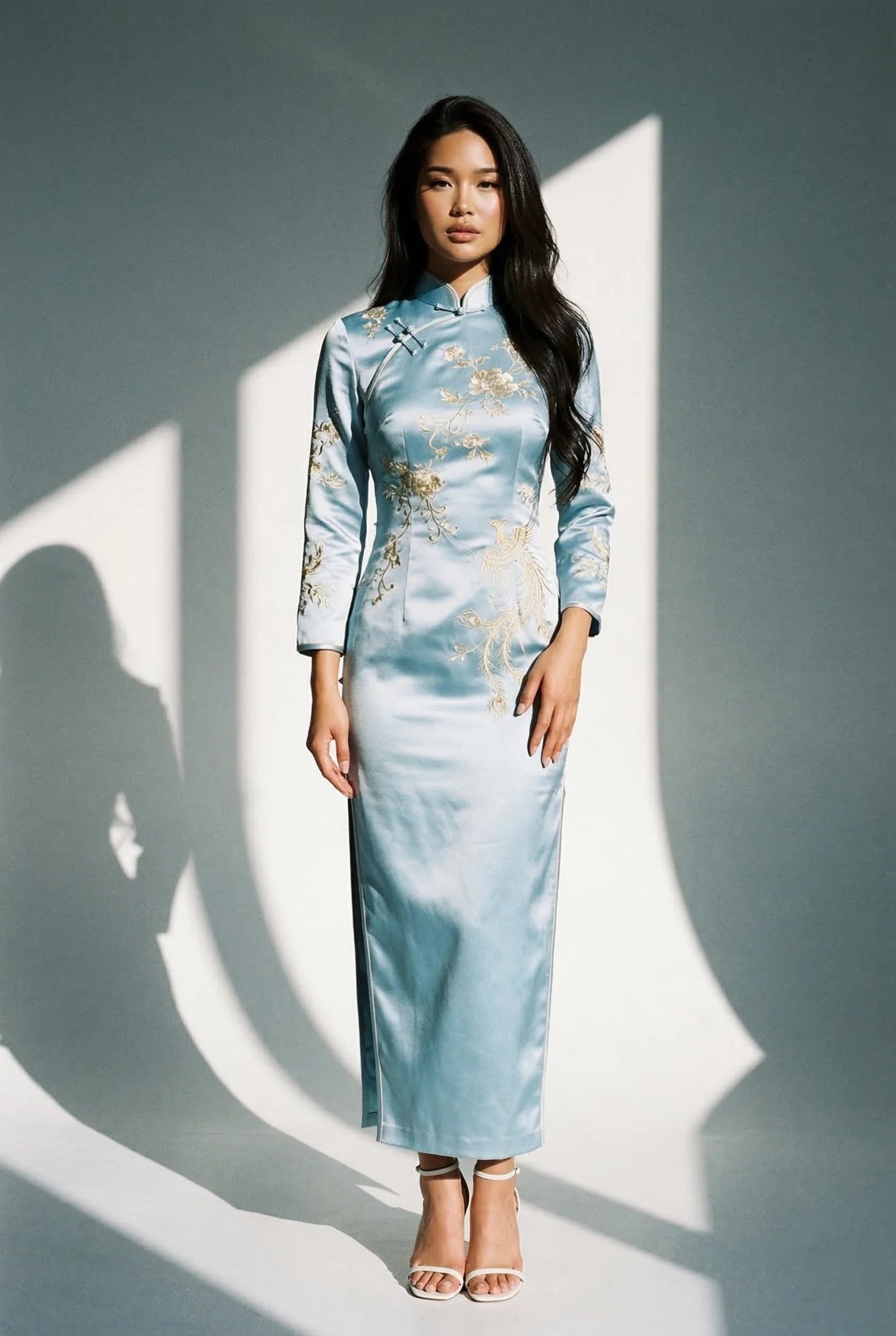 Model in a light blue silk qipao with gold embroidery by Maison Hua, demonstrating the two-finger rule for collar comfort and professional silk care