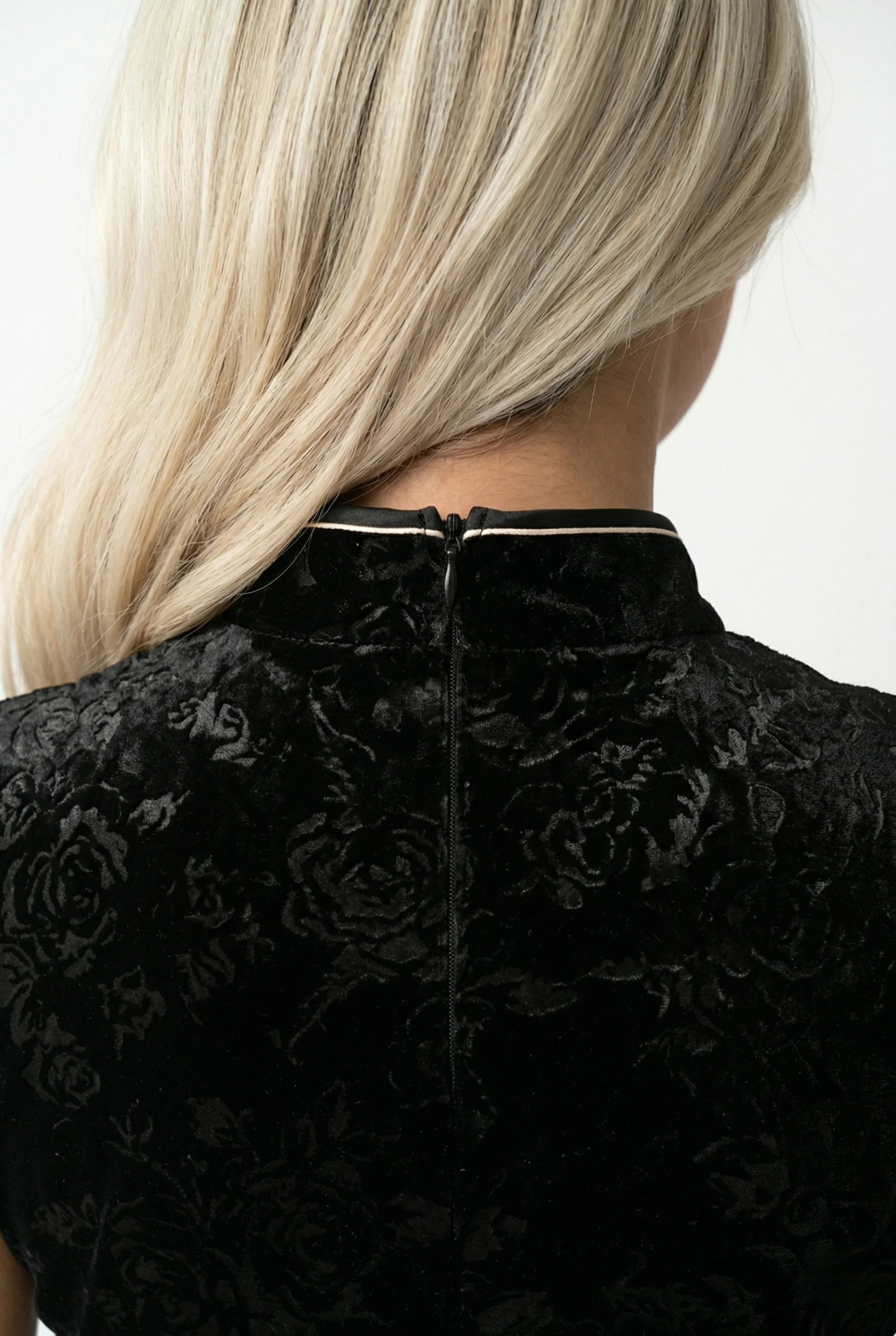 Detail view of the mandarin collar and back zipper on the black velvet dress.