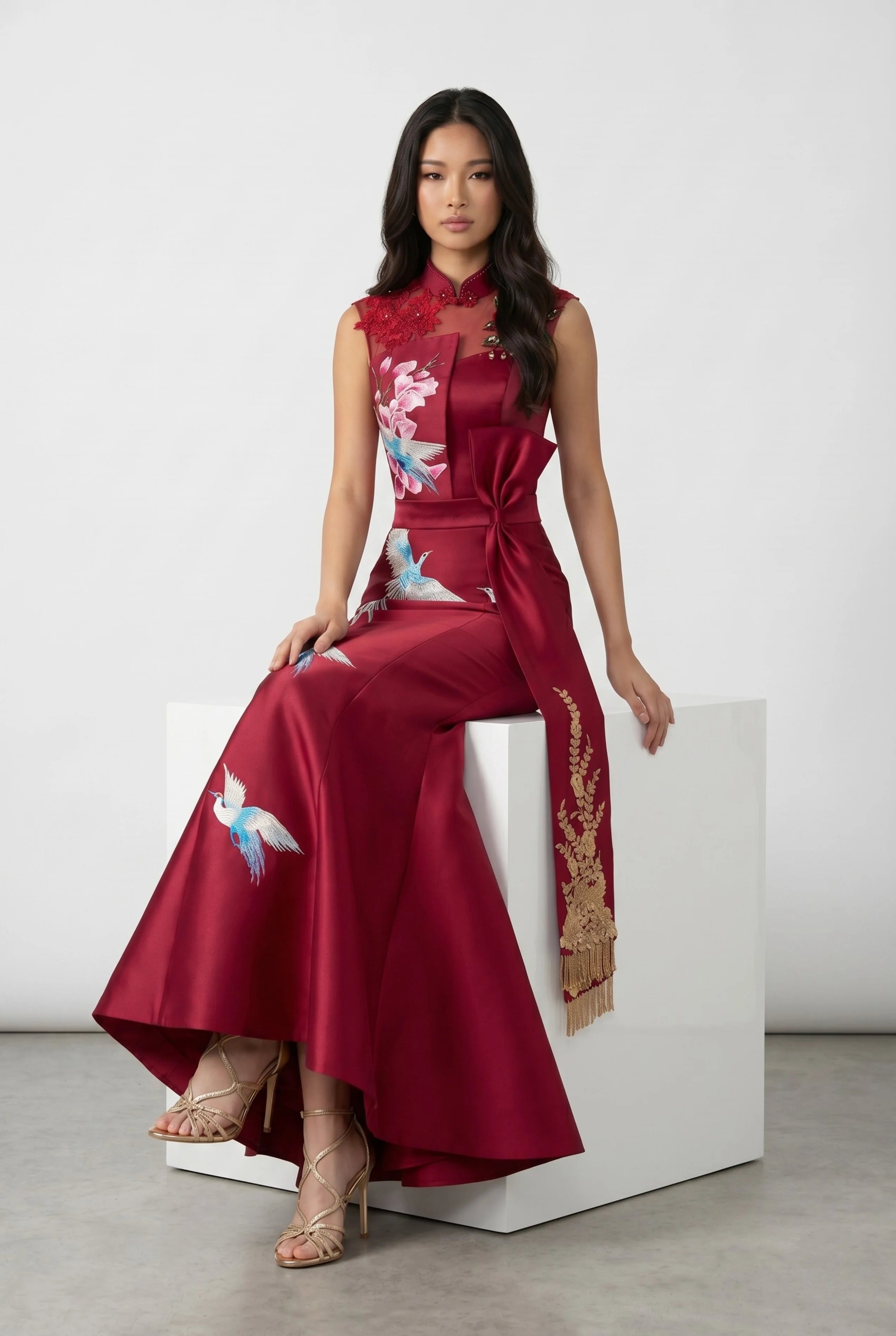 Full-body view of a woman sitting on a white block cube, elegantly displaying the drapes of the red mermaid qipao