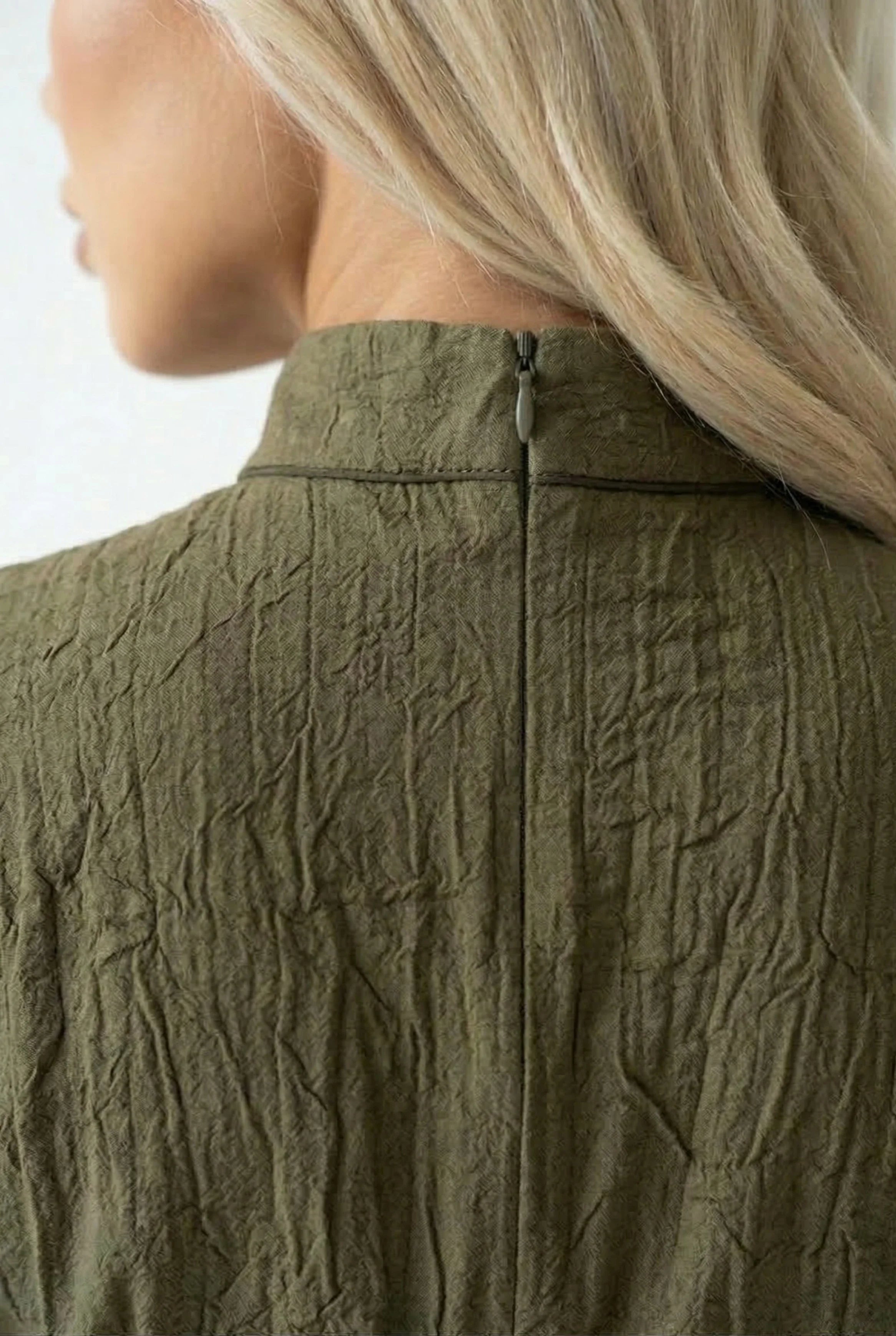 Detail shot of the high mandarin collar and back zipper on an olive green textured fabric dress.