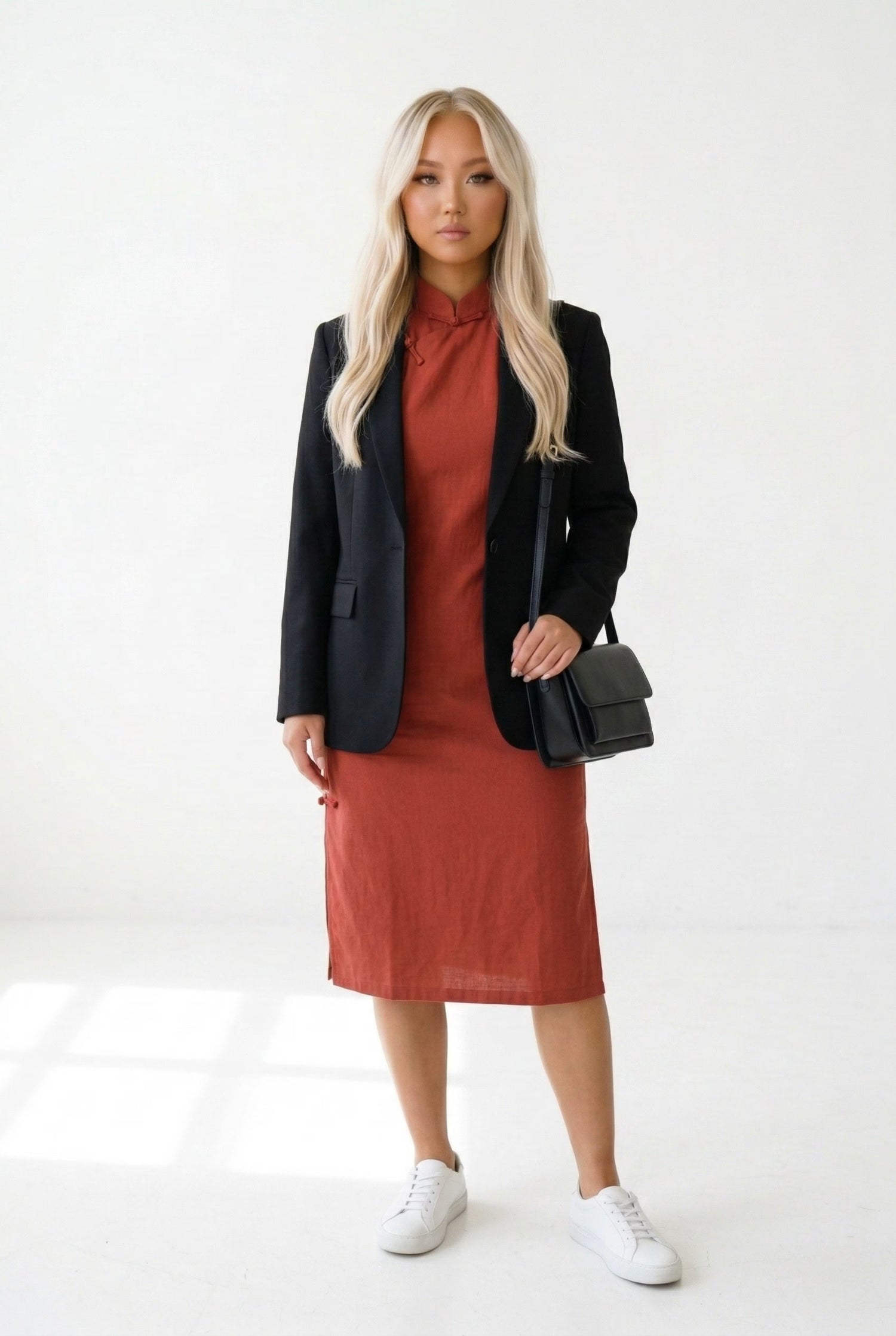 Modern styling of a red qipao dress paired with a black blazer and sneakers for an urban professional look