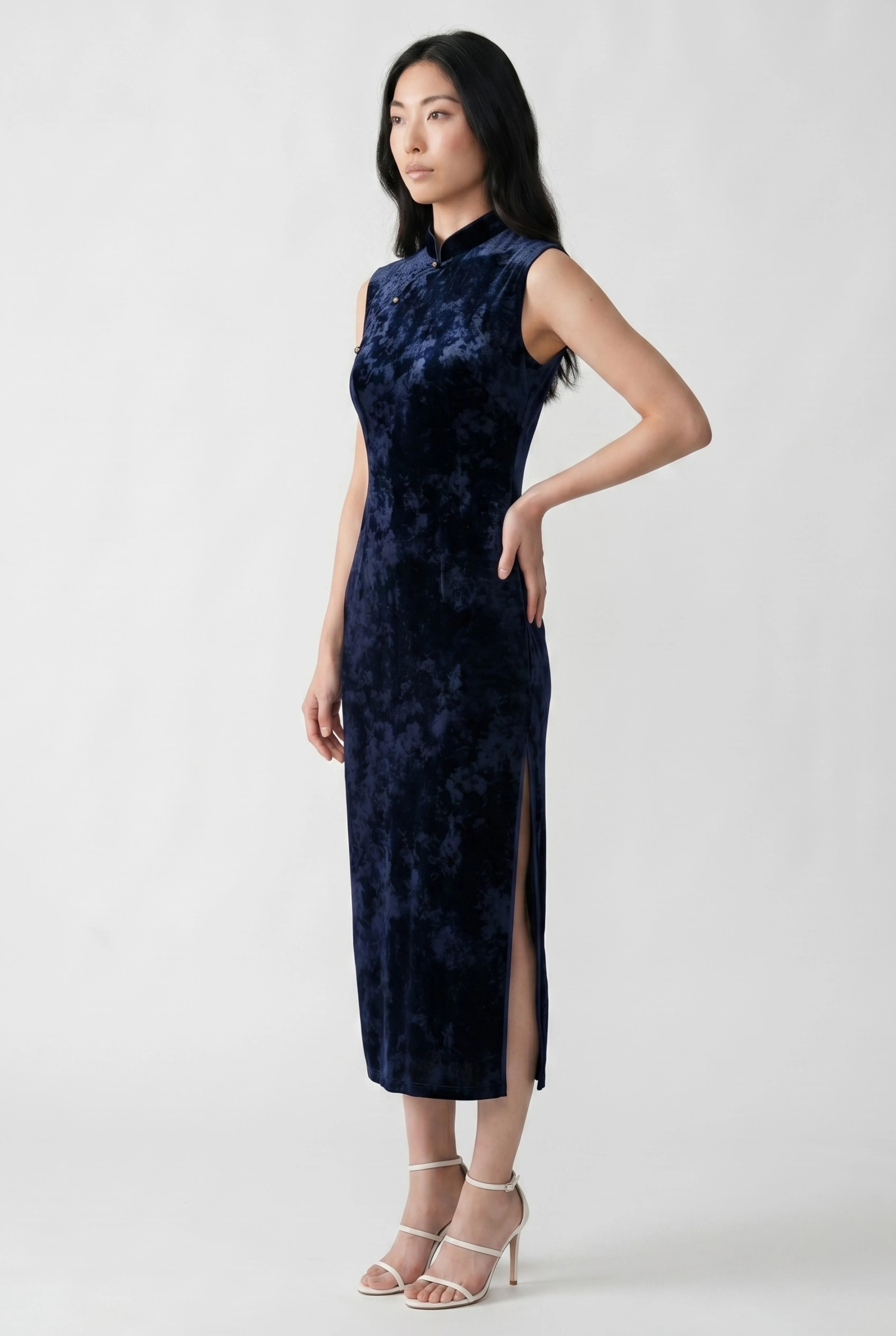 Three-quarter side profile view of a woman posing in a navy blue velvet qipao, showcasing the side slit