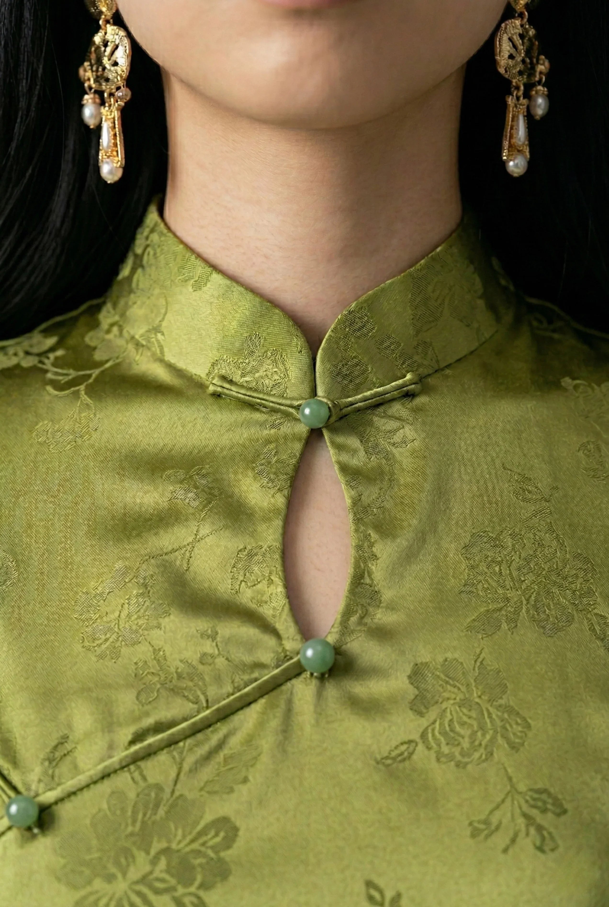 Close-up of the mandarin collar and keyhole neckline on an olive qipao