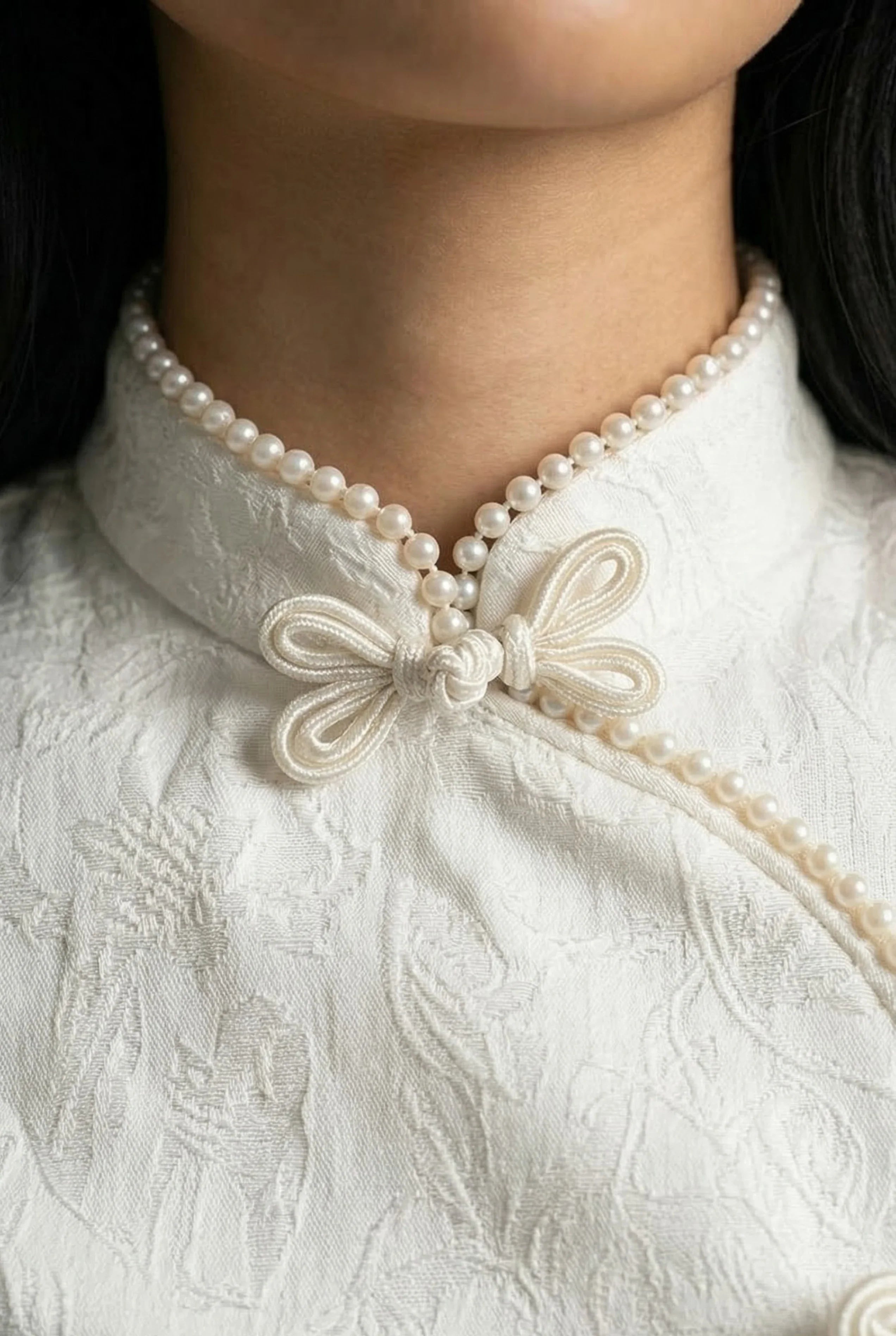 Extreme close-up of the pearl-trimmed mandarin collar and ivory butterfly frog button on a white Qipao romper.