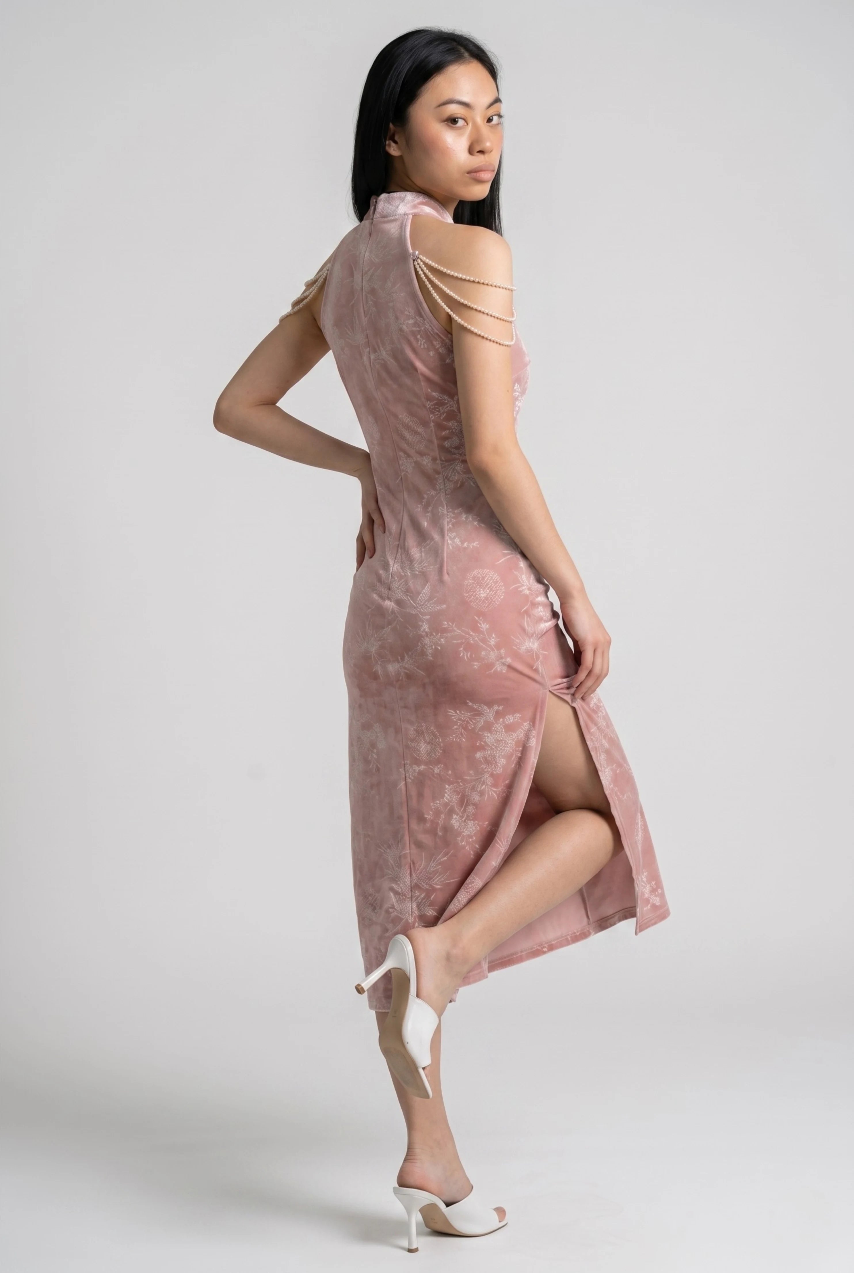 Side view of a woman lifting her leg in the pink velvet qipao dress, showing the high side slit