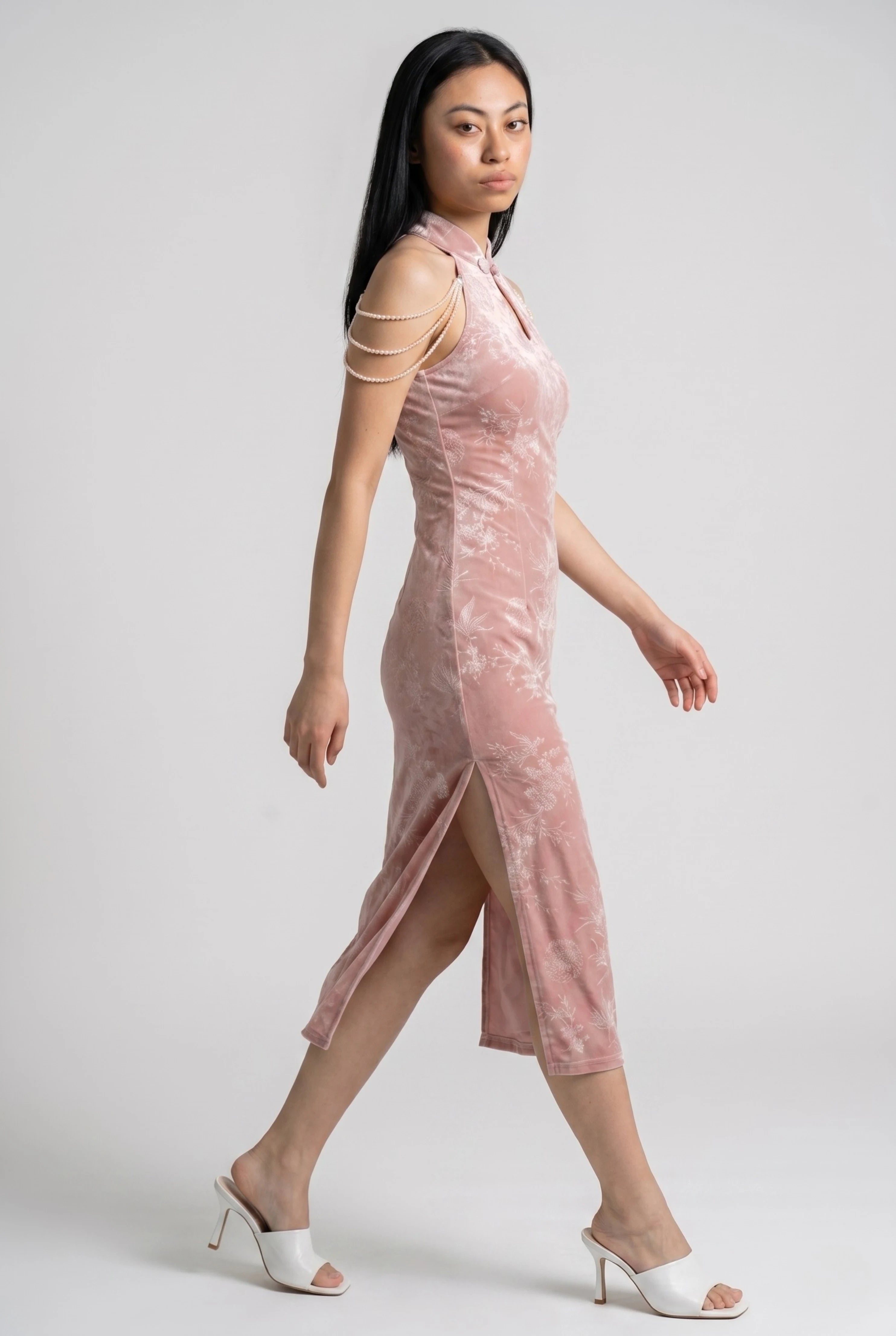 Side profile view of a woman walking in a pink velvet qipao dress, highlighting the side slit