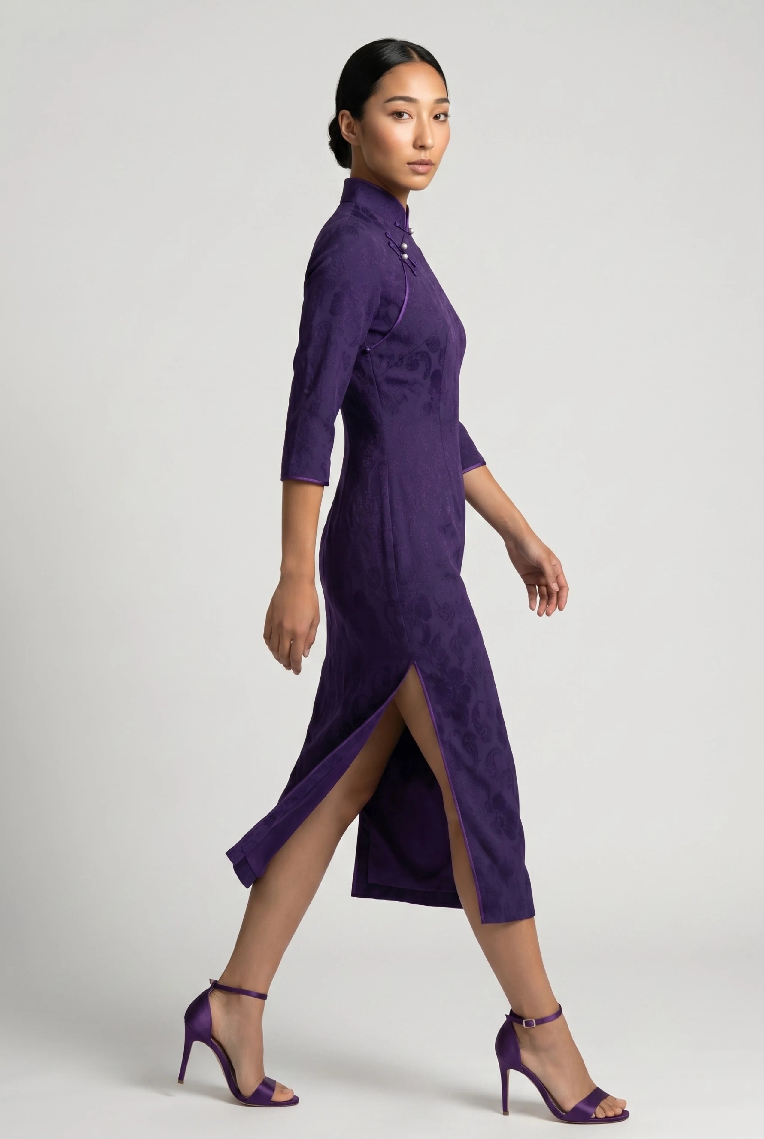 Side profile view of a woman walking in the purple velvet cheongsam dress, showcasing the high side slit