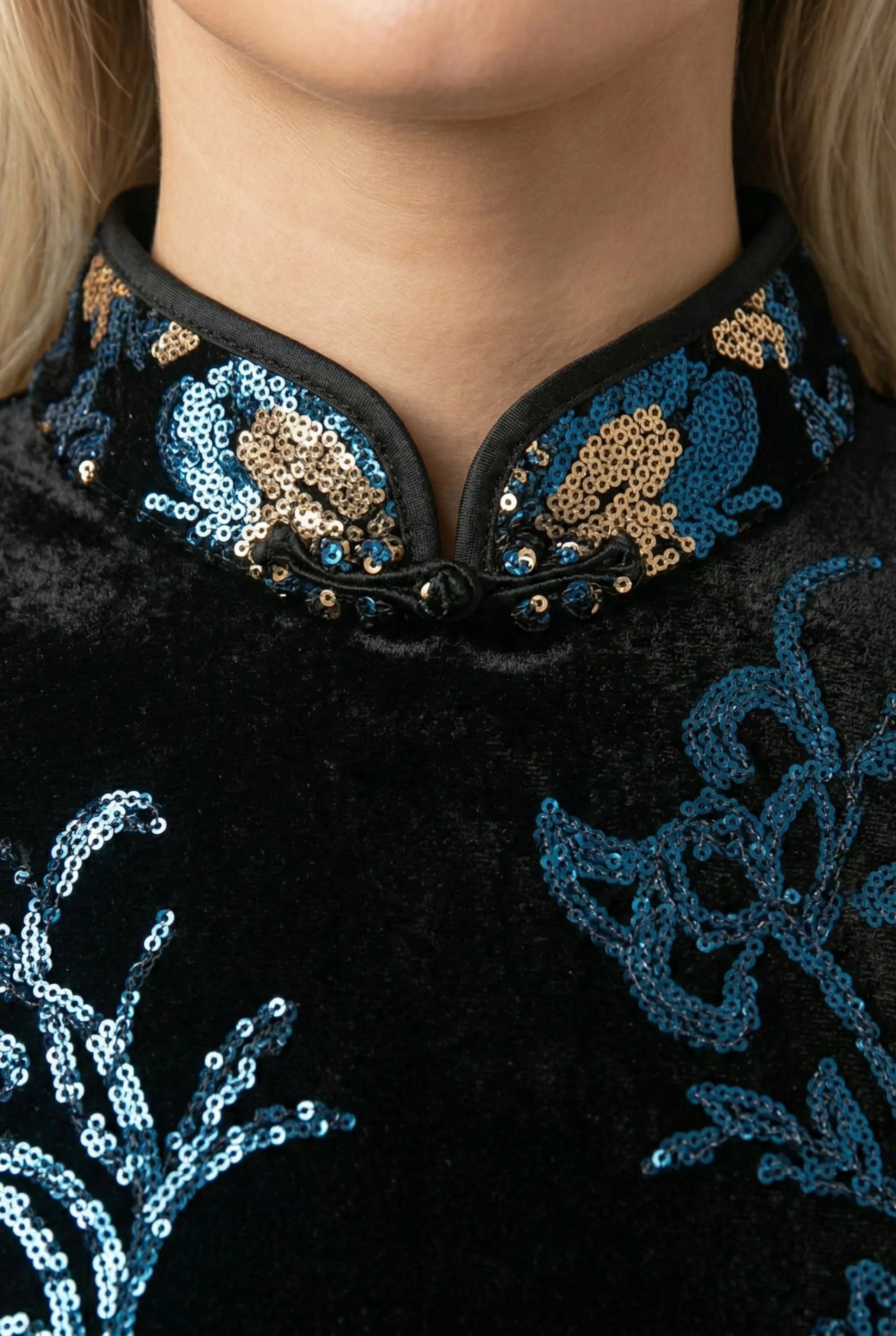 Close-up of a black velvet qipao showing the traditional mandarin collar and intricate blue and gold sequin floral embroidery