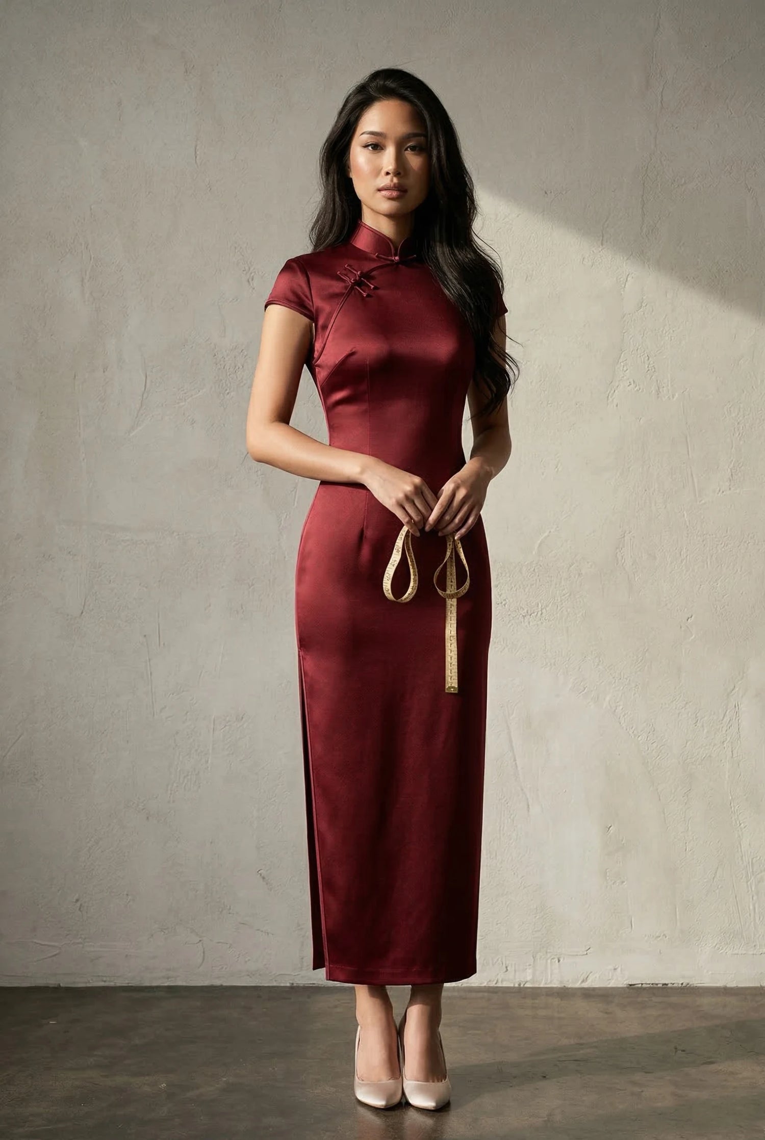Model in a burgundy silk qipao holding a measuring tape by Maison Hua, illustrating the professional fit and iconic straight-line drape of high-grade non-stretch silk