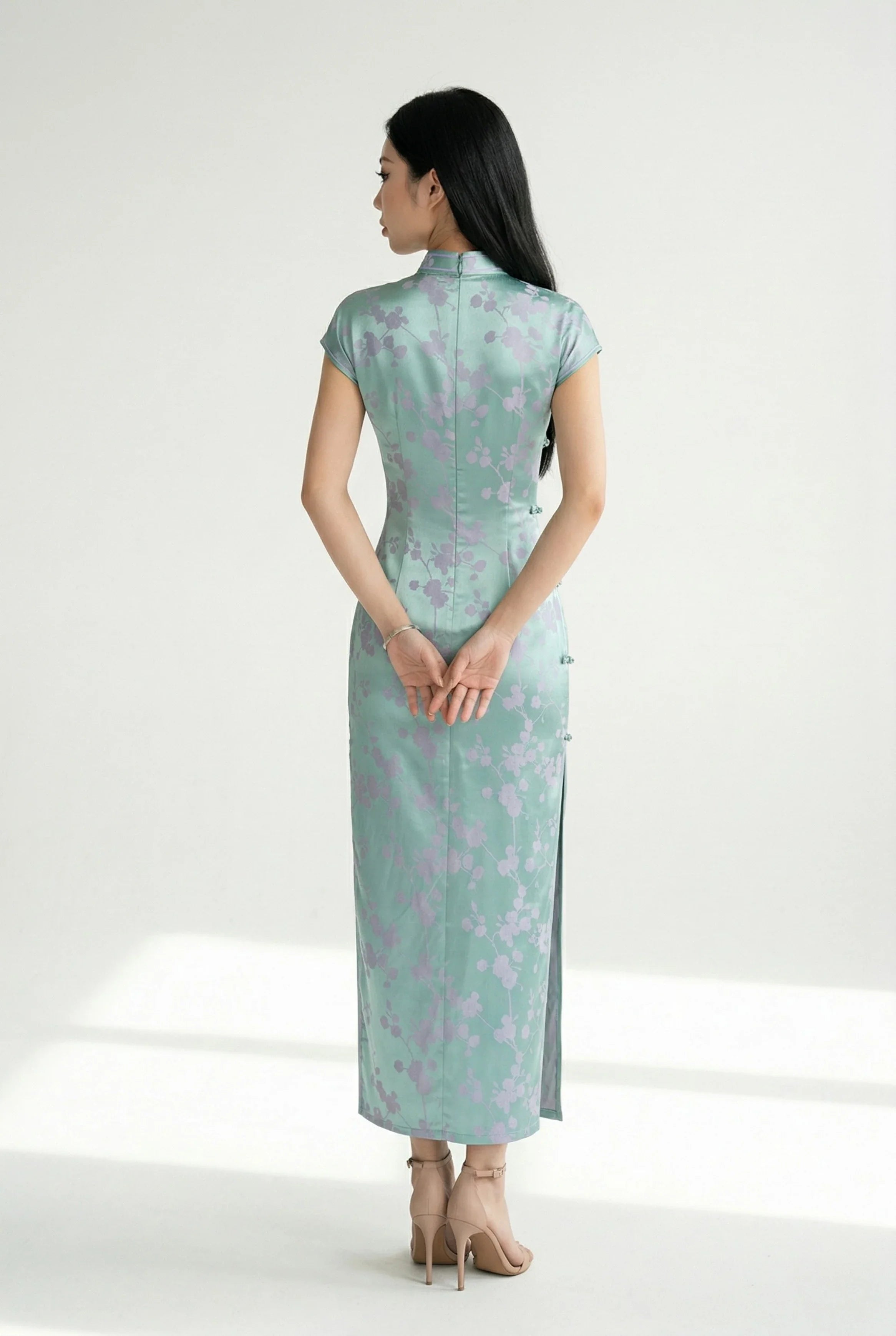 Back view of the silky jade-green cheongsam, hands behind back.