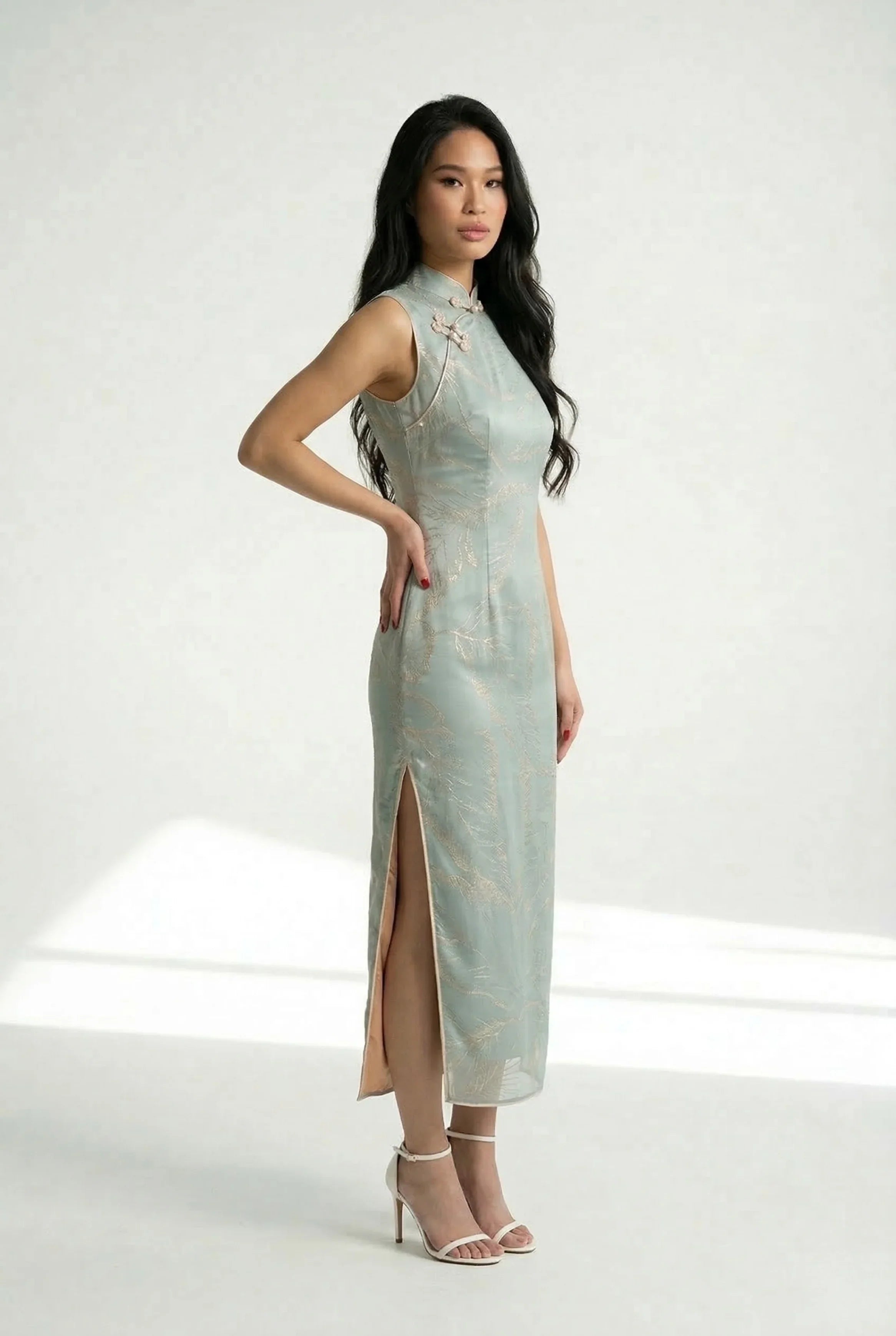 Side profile of a sleeveless blue Chinese dress highlighting the high side slit and the refined gold leaf detail on the fabric.