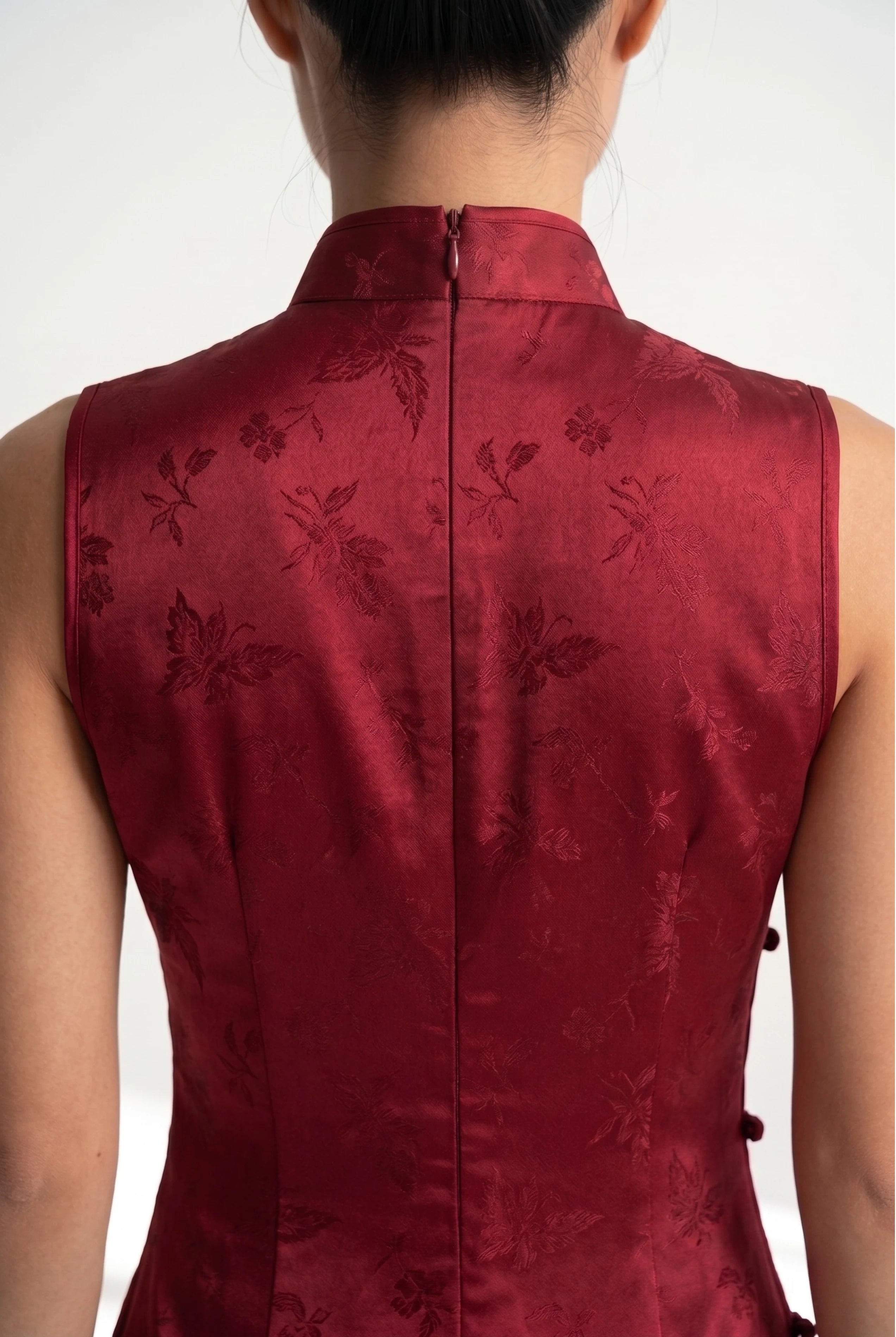 Close-up front view of the high mandarin collar and matching traditional frog buttons on the sleeveless red qipao