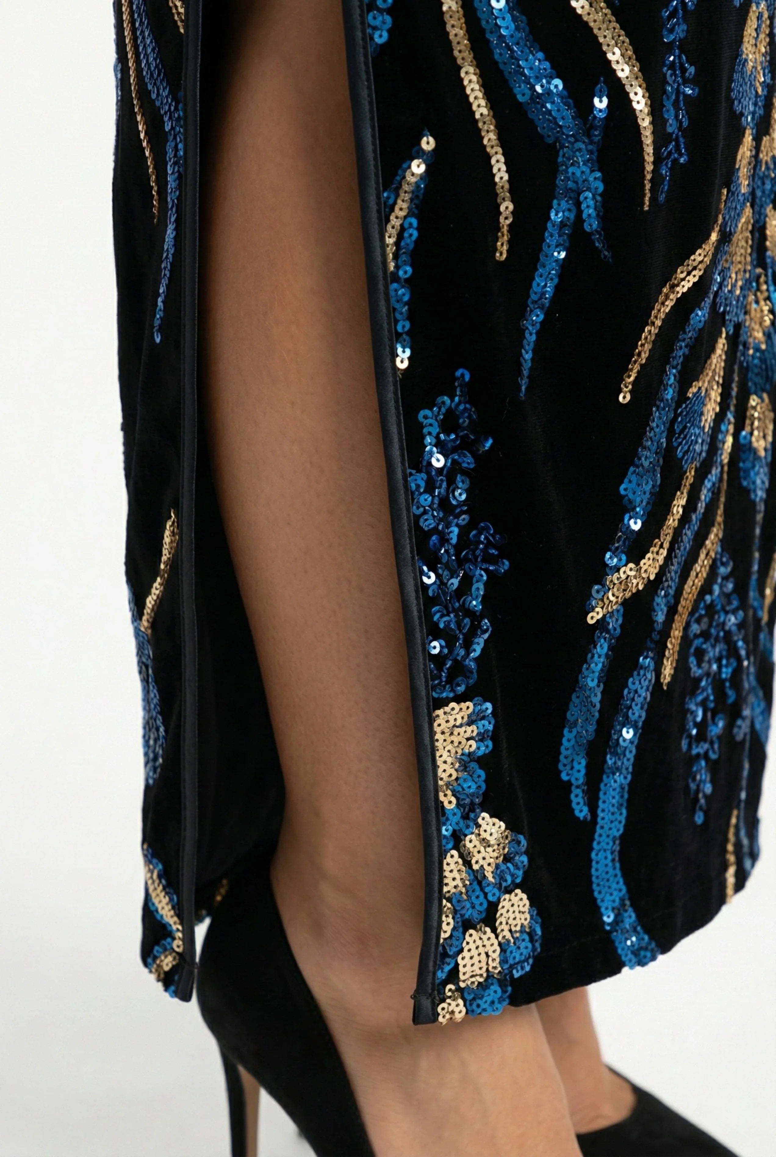 Close-up of the high side slit and bottom detail of a black velvet cheongsam dress with blue and gold sequin flowers