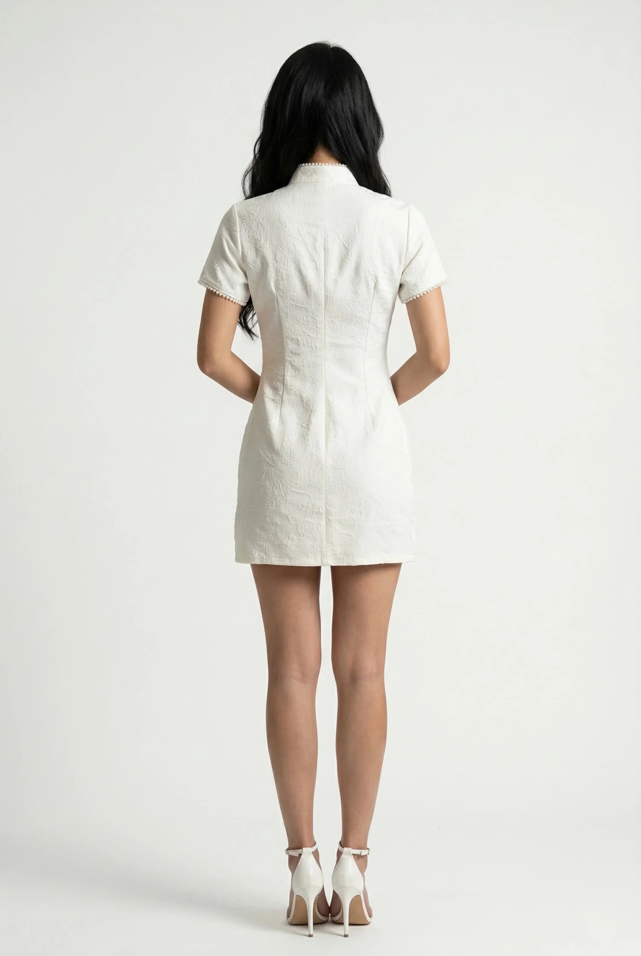 Back view of a form-fitting white playsuit with a traditional mandarin collar and elegant pearl detailing.