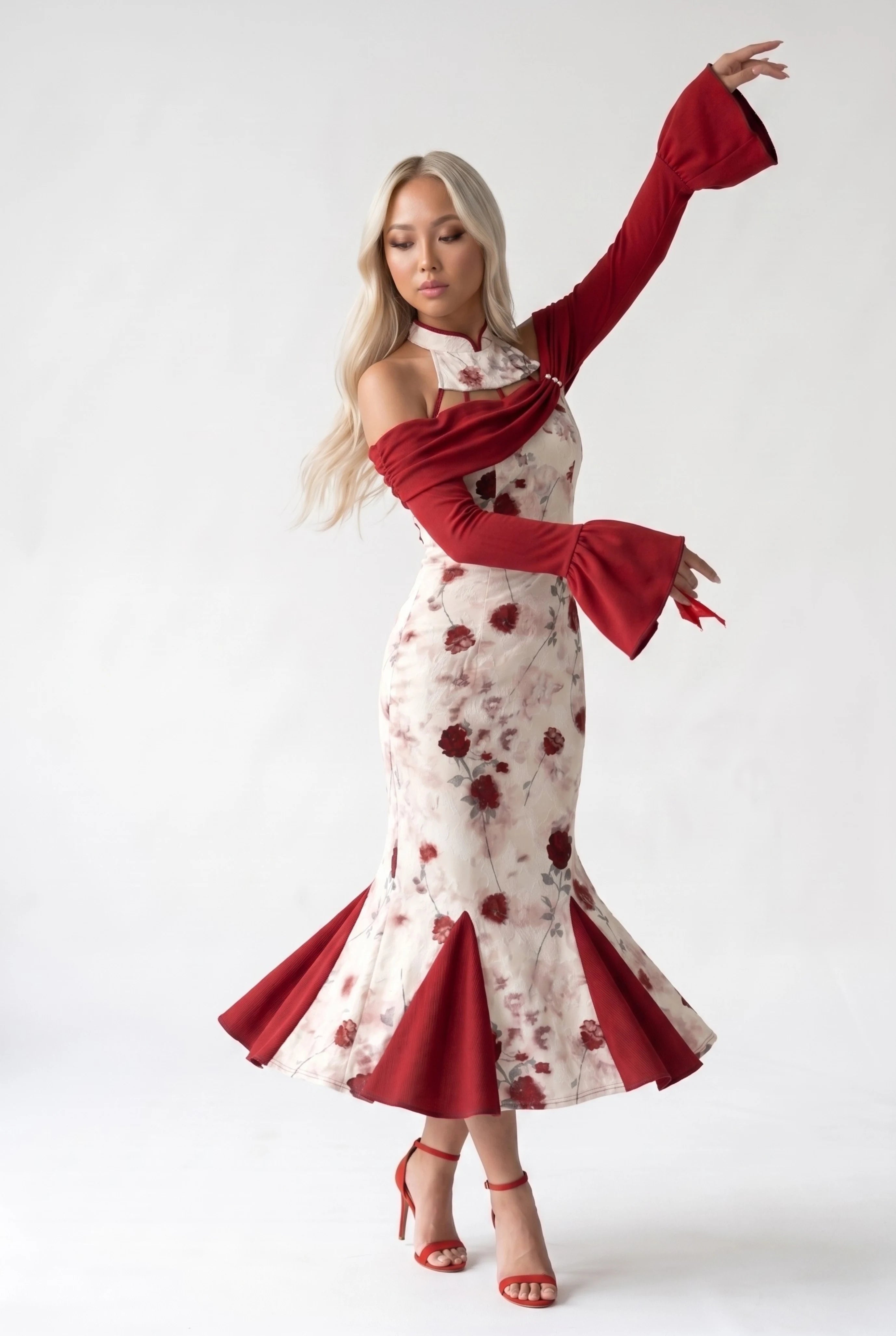 Full-body front view of a woman posing dynamically with raised arms, highlighting the flowing red sleeves of the floral qipao