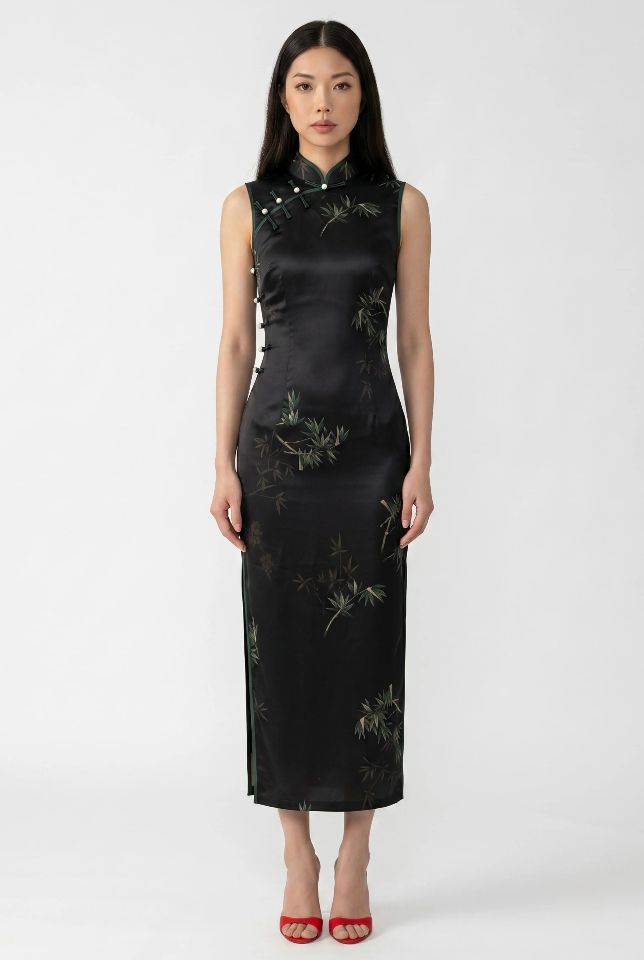 Front full-length view of a sleeveless black satin women qipao with a green bamboo pattern and red heels