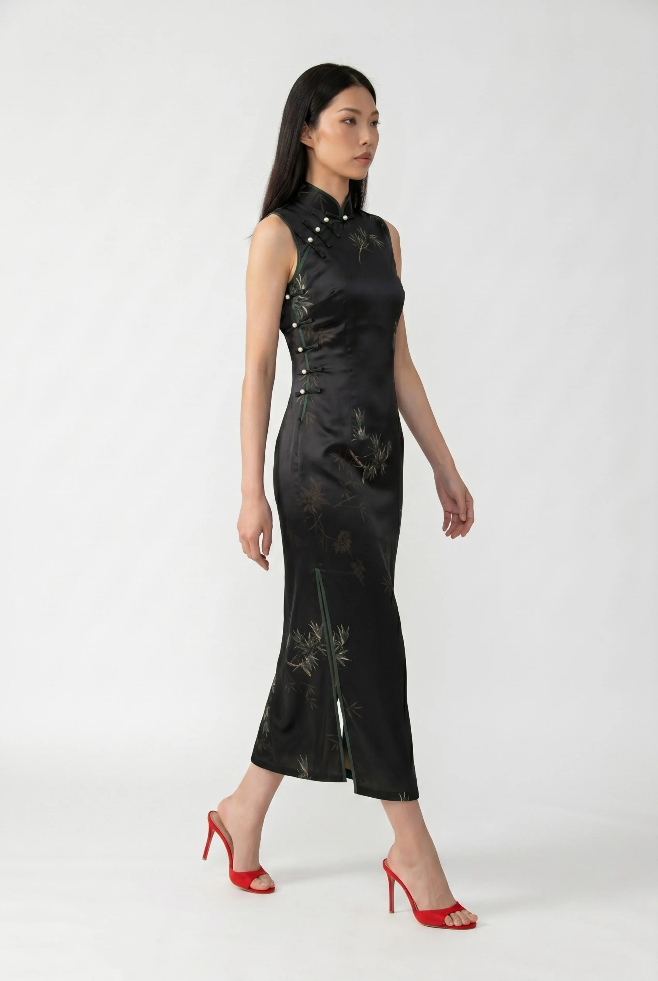 Side profile view of a woman walking in the black qipao dress, showcasing the high side slit and red heels