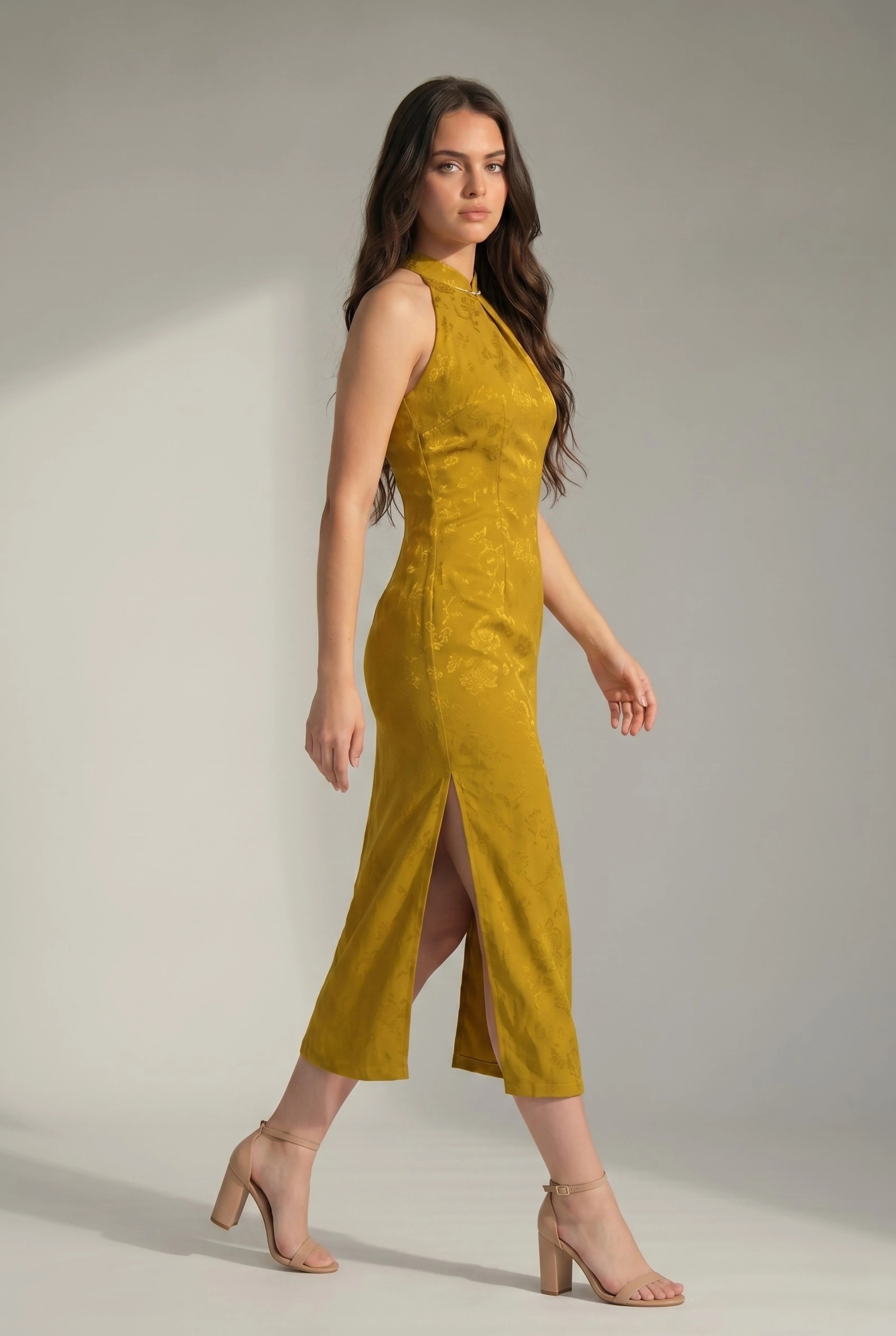 Side view of a woman walking in a yellow qipao dress, showcasing the high side slit and nude heels