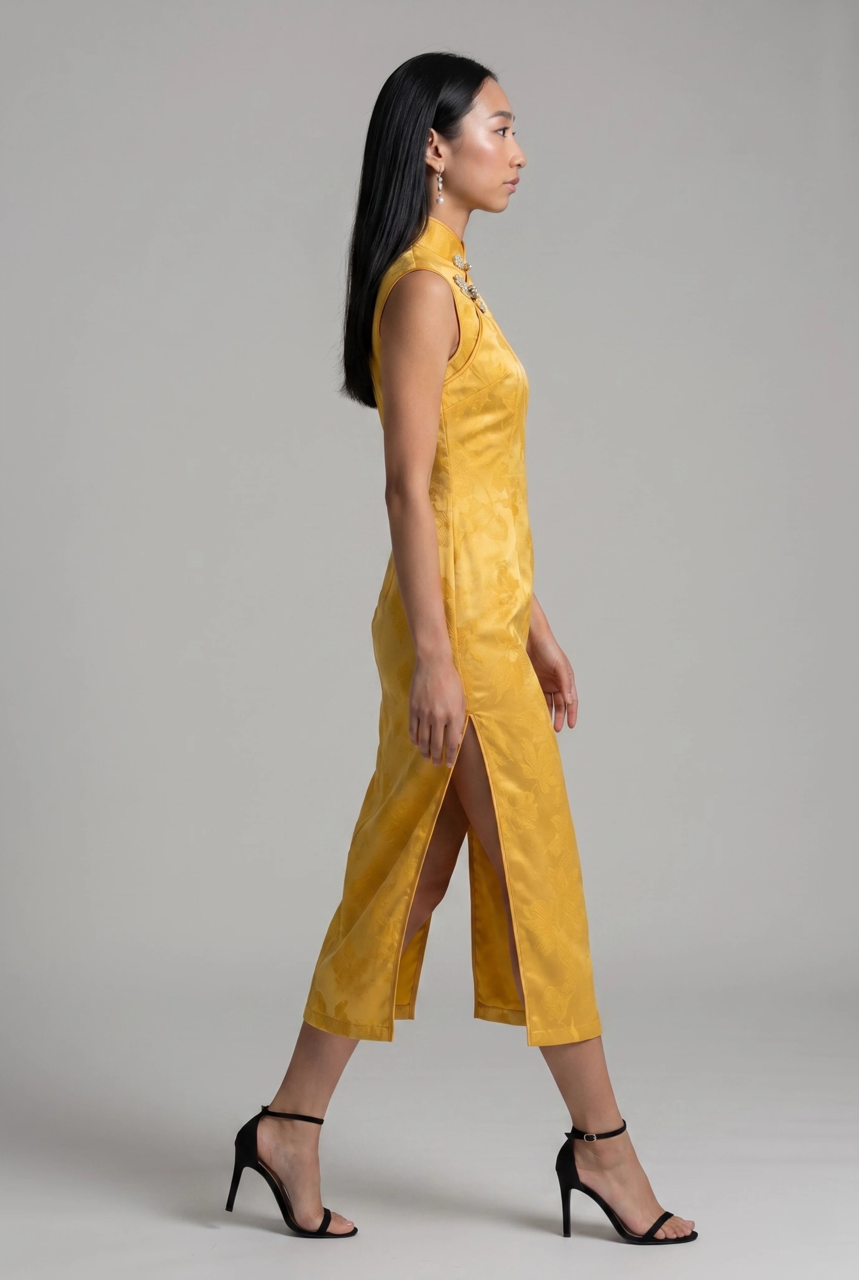 Full-body side profile view of a woman standing in the yellow velvet cheongsam dress